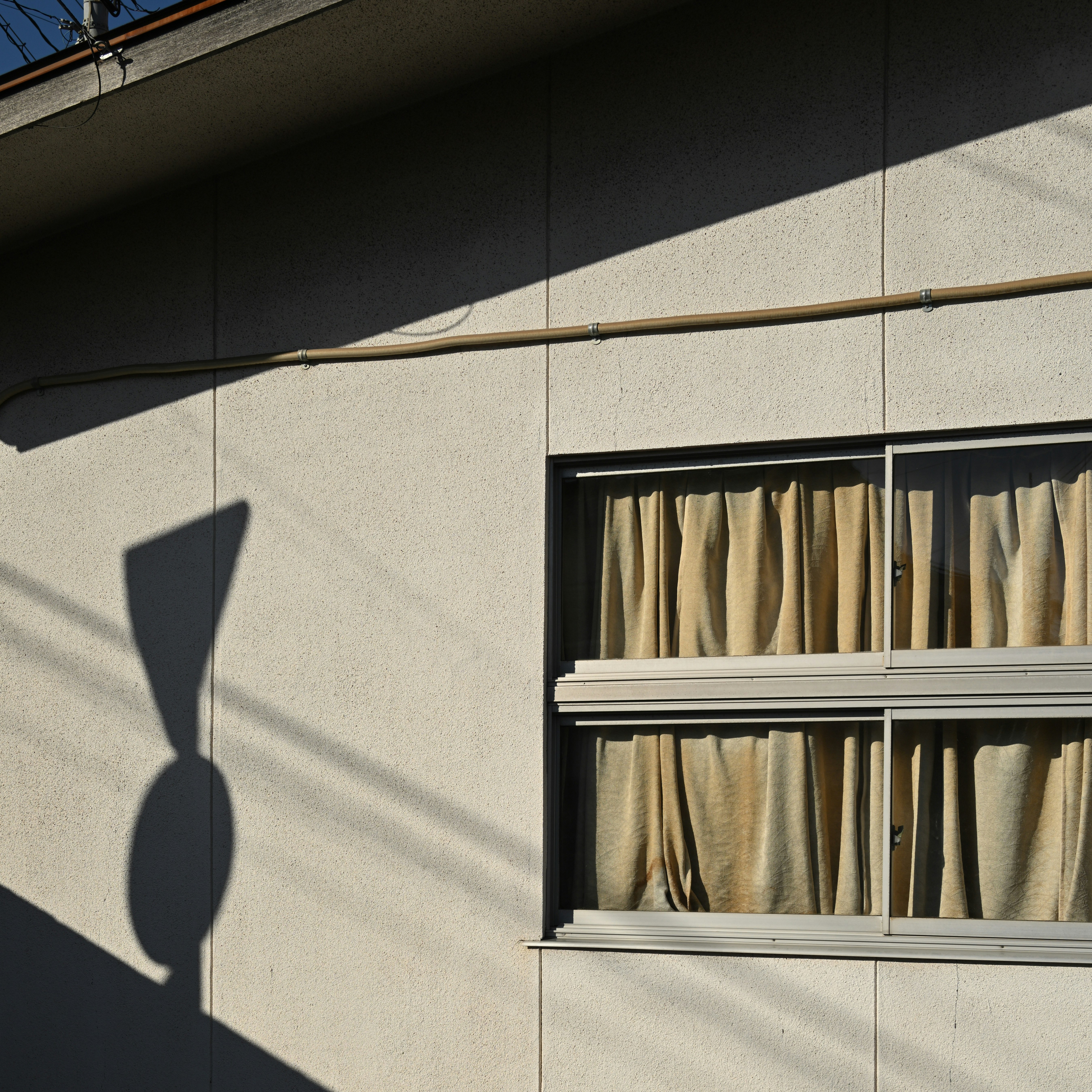窓辺の壁に落ちる影とカーテンのある建物