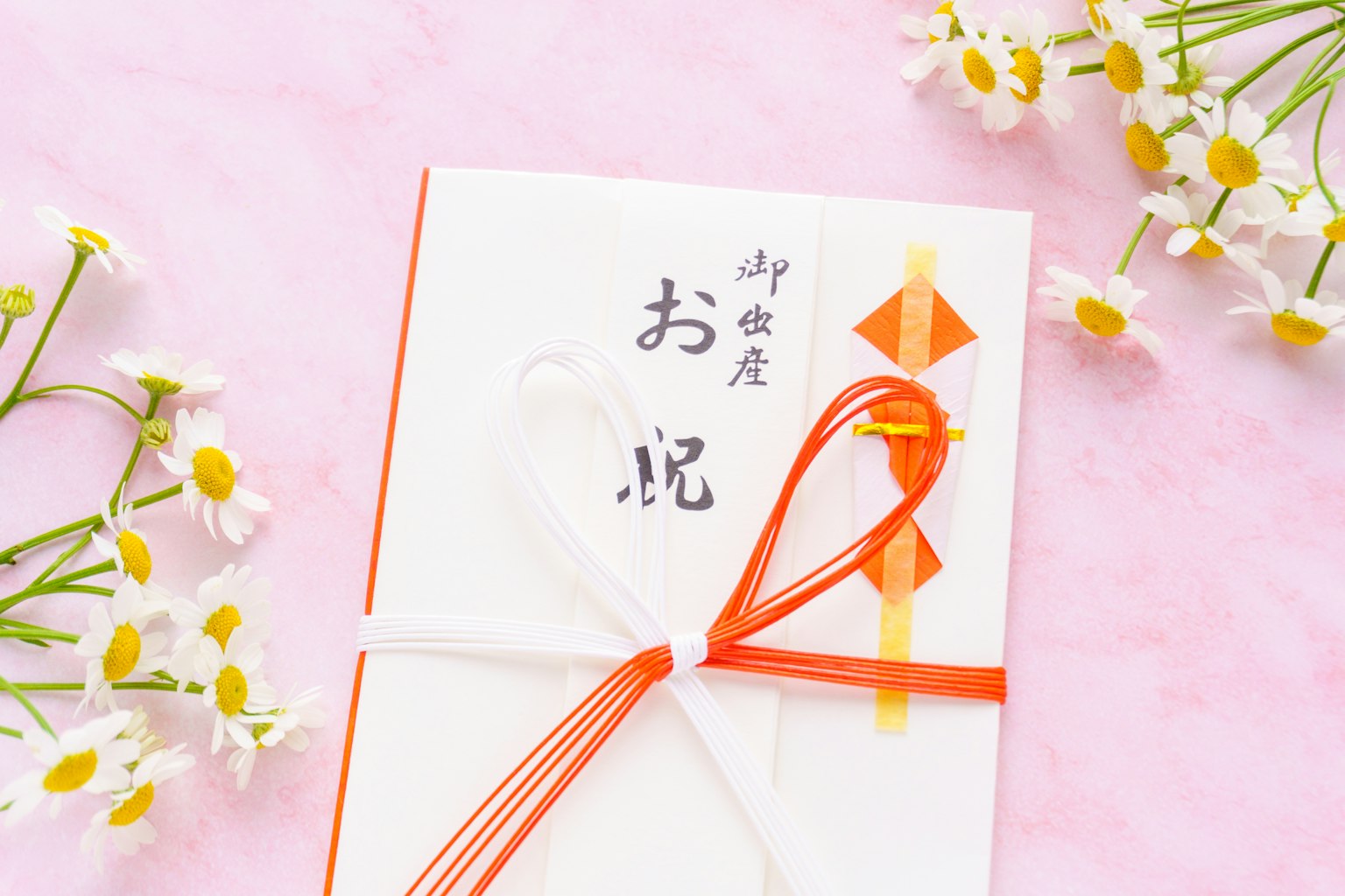一个用红白丝带绑着的白色信封，旁边有小花和庆祝卡片