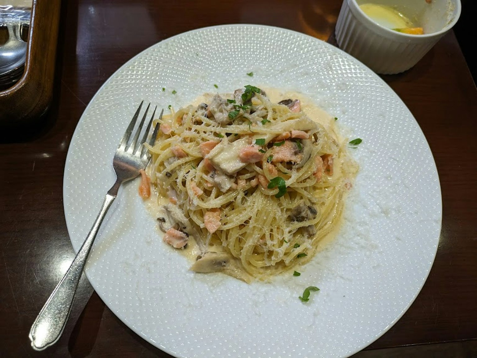 Piatto di spaghetti con salsa di panna guarnito con erbe e una forchetta di lato