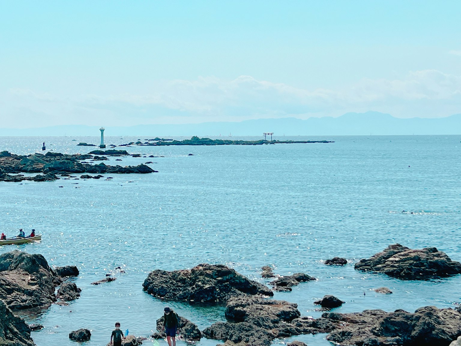 Escena costera con mar azul y rocas dispersas con personas disfrutando de la playa