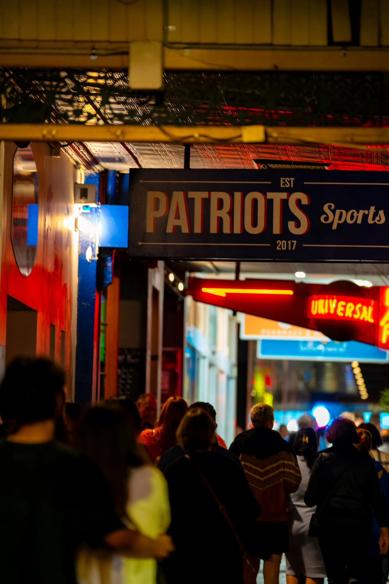 Escena de calle concurrida con el cartel Patriots Sports