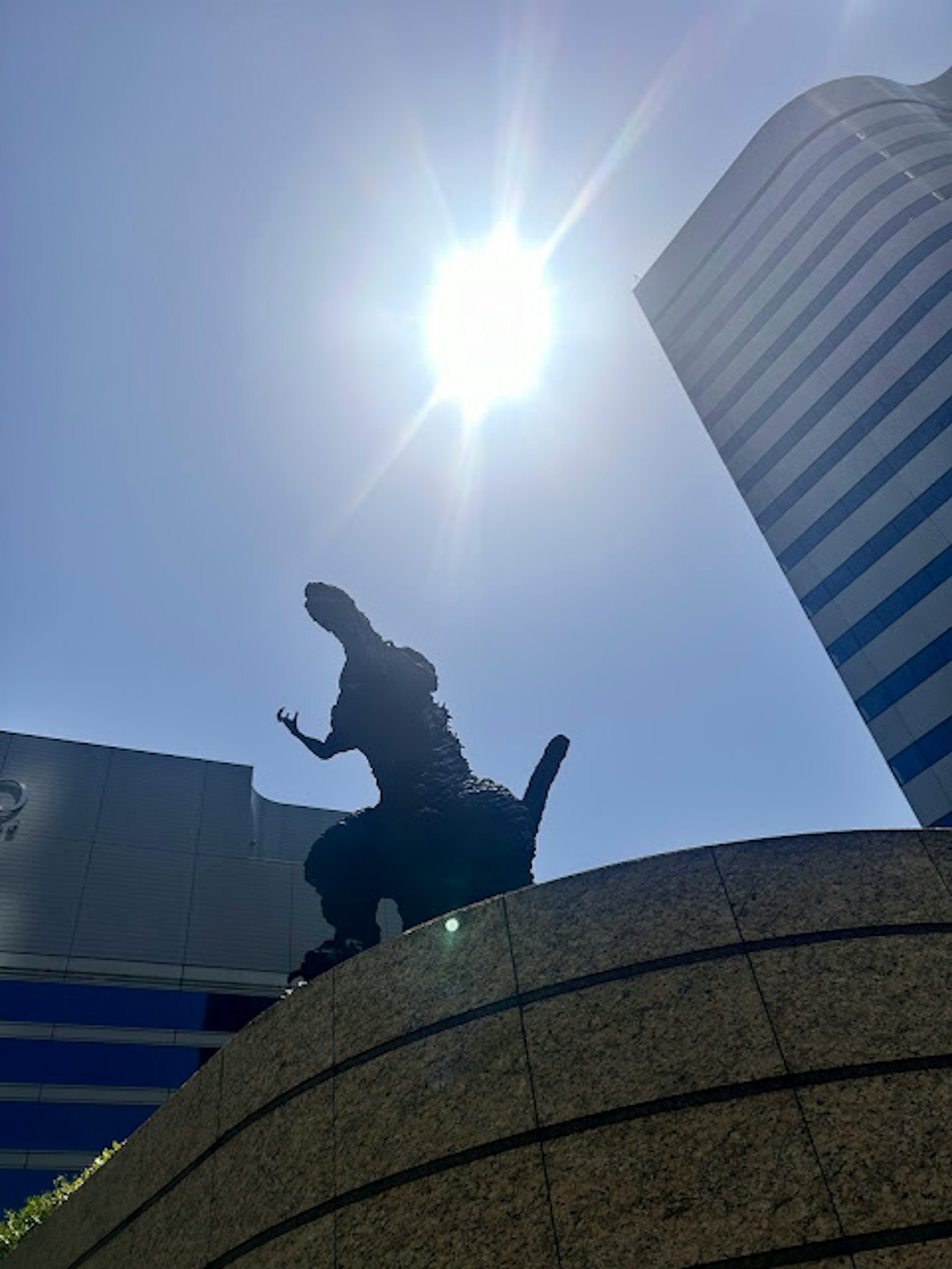 背對太陽的哥斯拉雕像輪廓與現代建築背景