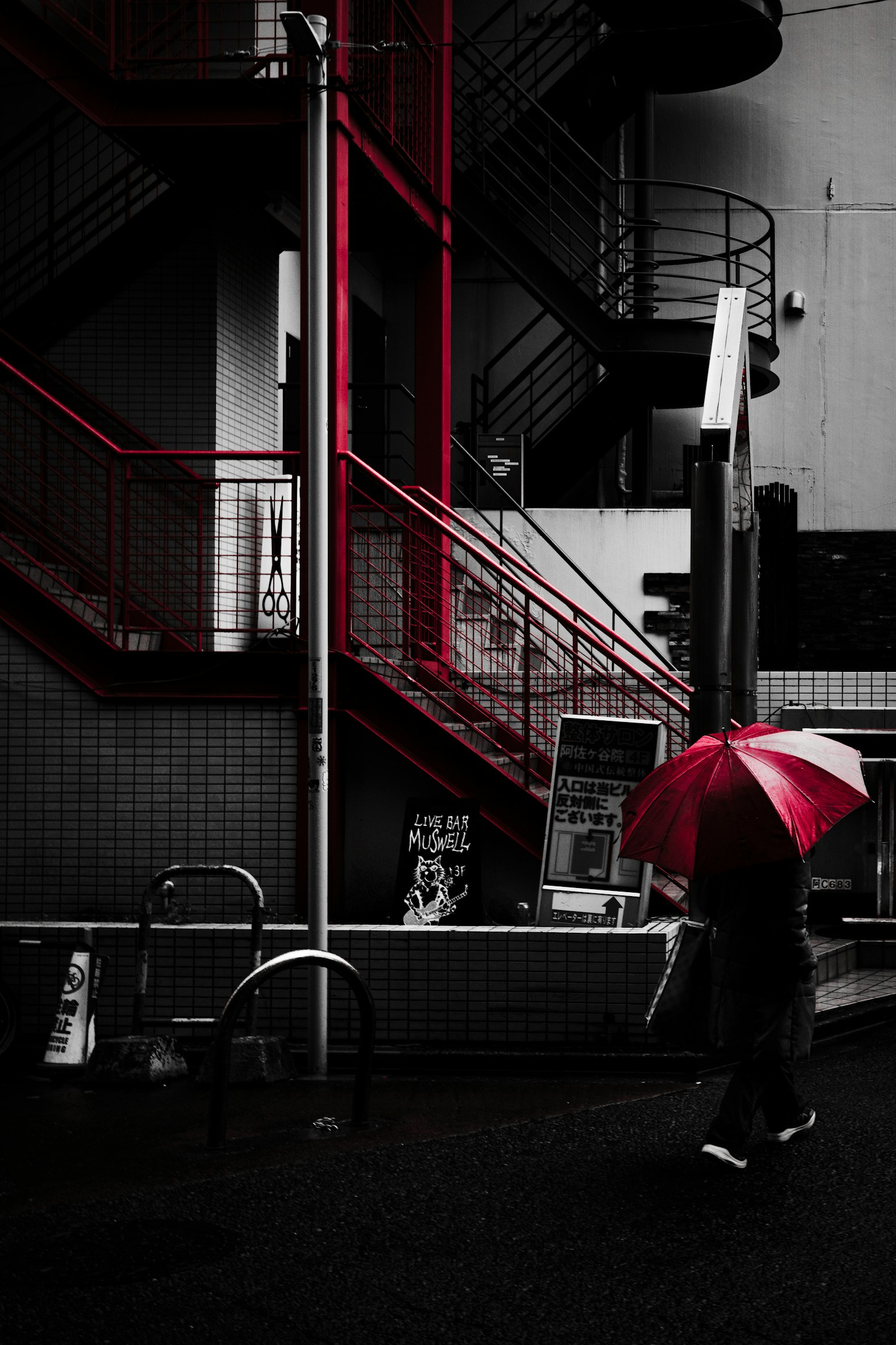 赤い傘を持った人物が階段の近くを歩いているモノクロの風景