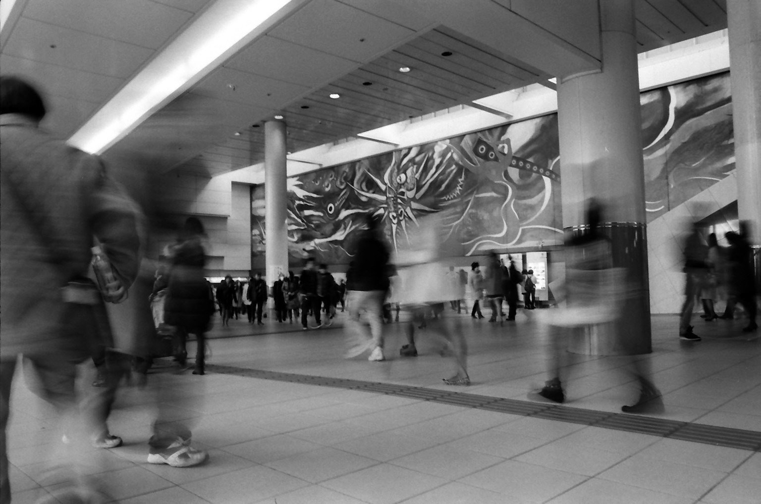 Image en noir et blanc d'un hall moderne animé avec une grande fresque