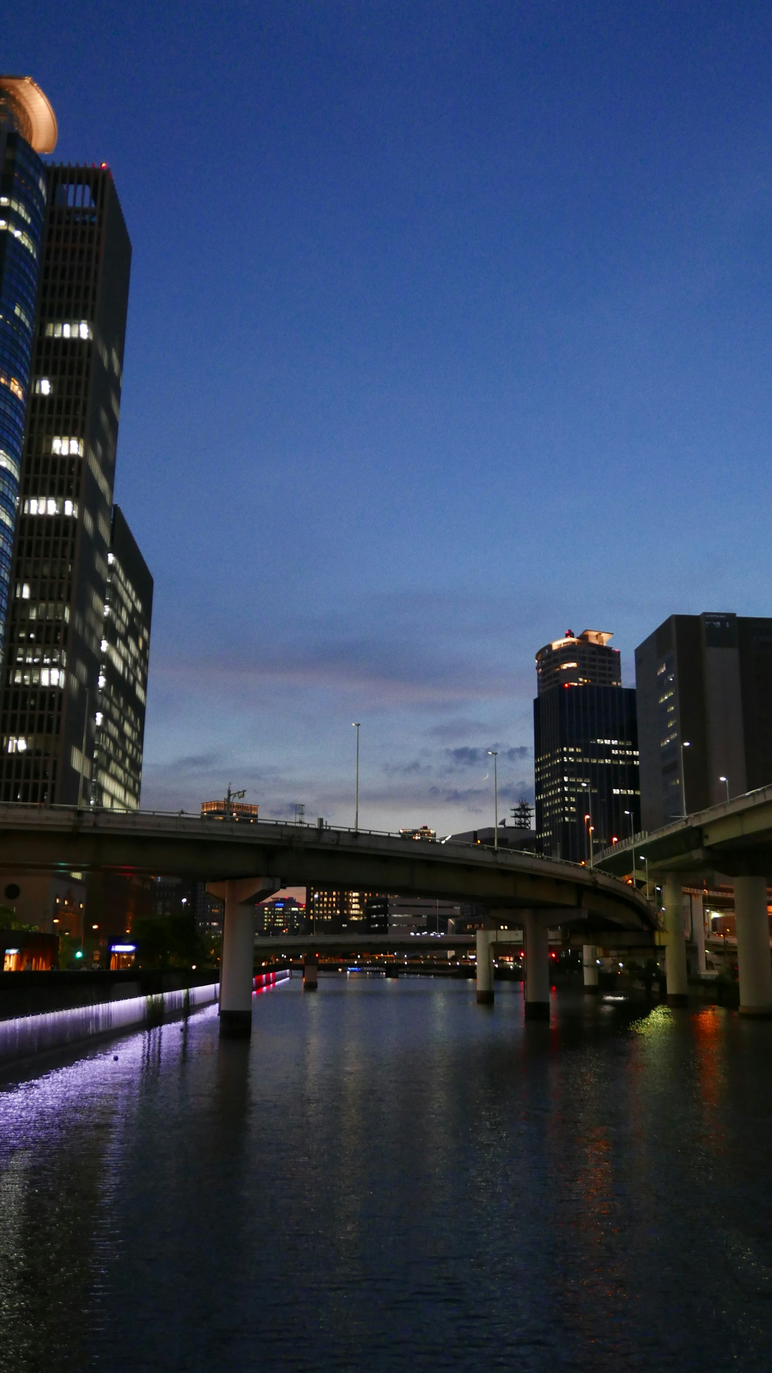 Pemandangan kota malam dengan sungai dan jembatan dikelilingi gedung pencakar langit