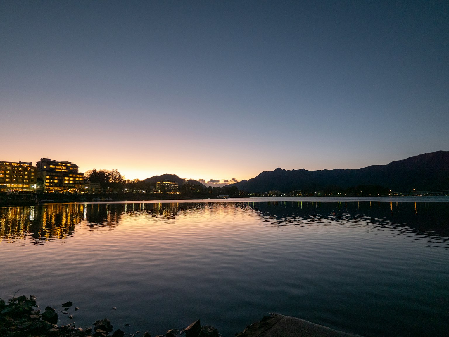 Paisaje de atardecer junto al lago con montañas y reflejo en el agua edificios