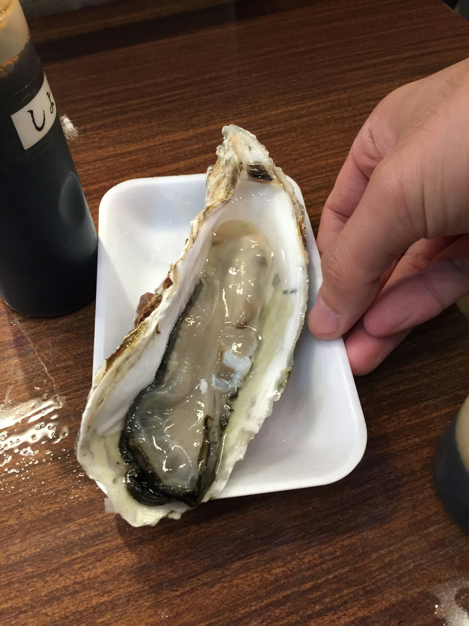 一只大生蚝被拿在白色盘子上方