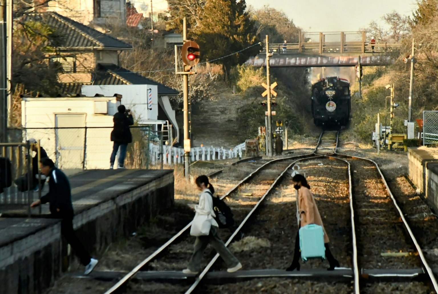 ผู้คนรออยู่ที่ชานชาลารถไฟพร้อมนักท่องเที่ยวที่ข้ามรางรถไฟ