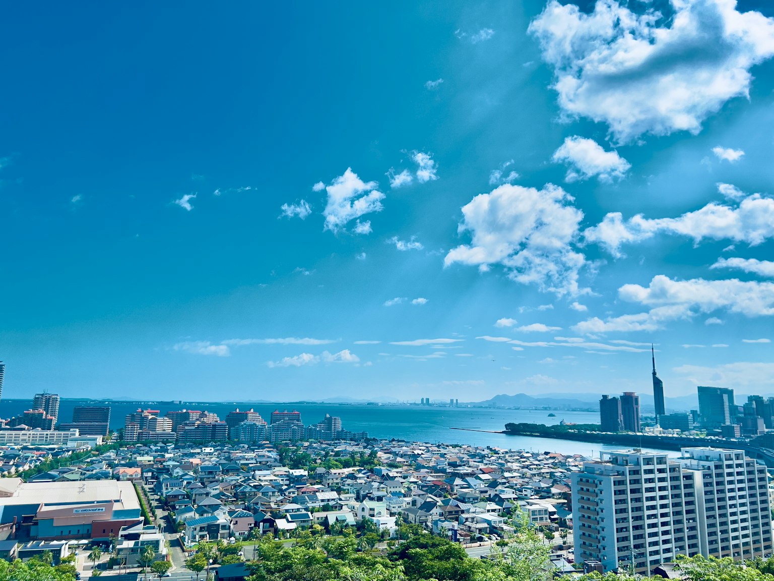 ทิวทัศน์เมืองกว้างที่มีท้องฟ้าสีฟ้าและเมฆมองเห็นทะเลและอาคาร