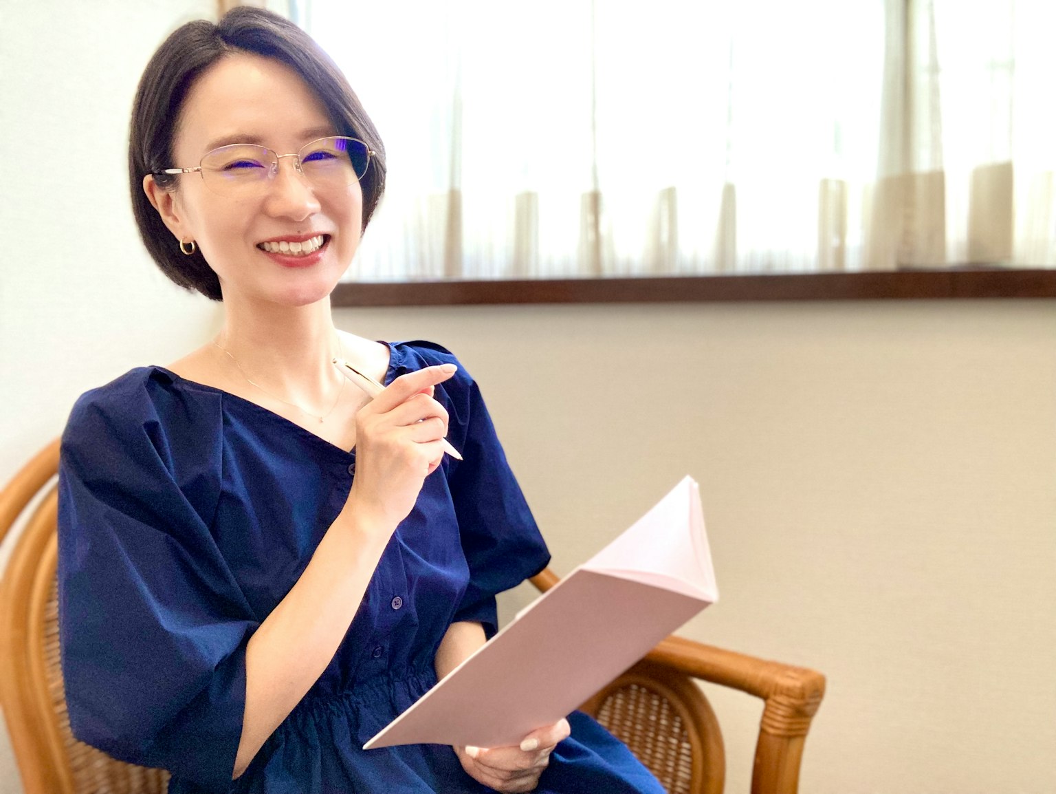 Joven mujer con vestido azul sonriendo mientras sostiene un cuaderno