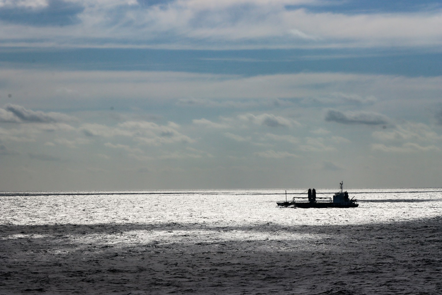 A boat on the shimmering sea under a cloudy sky
