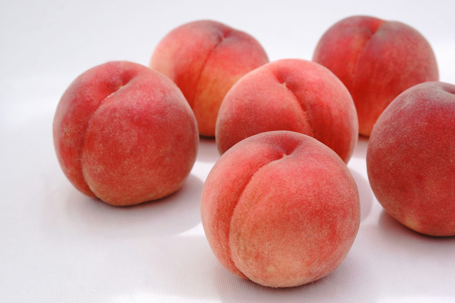 A close-up of six ripe peaches on a white background