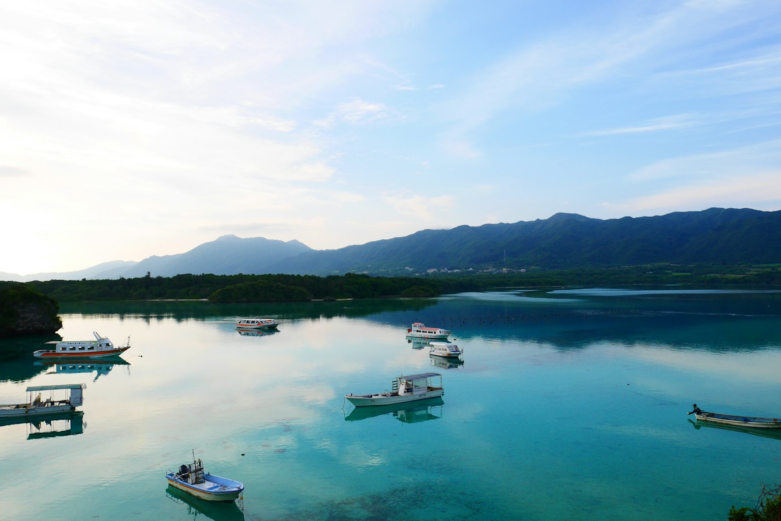 ทิวทัศน์ที่เงียบสงบของเรือที่ลอยอยู่บนผิวน้ำที่สงบพร้อมภูเขาในพื้นหลัง