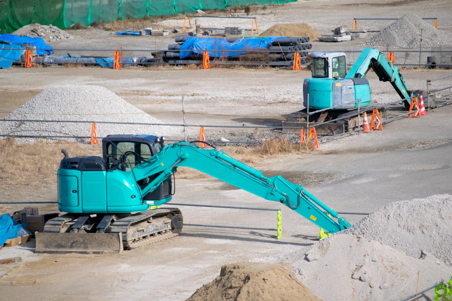 Due escavatori in un cantiere vicino a cumuli di sabbia