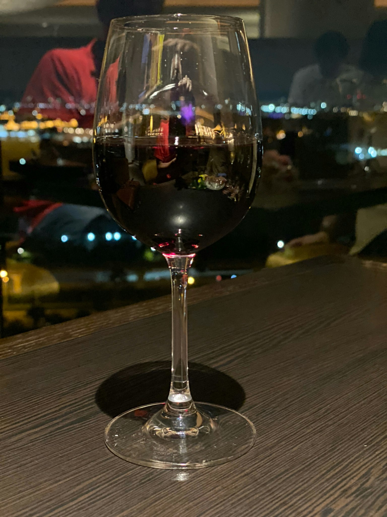 Una copa de vino tinto sobre una mesa reflejando una vista nocturna de la ciudad