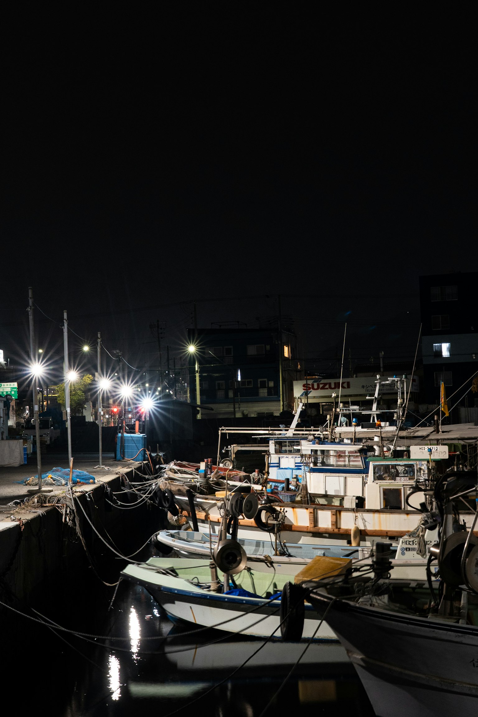Pemandangan pelabuhan malam dengan perahu nelayan bersandar cahaya memantul di atas air tenang
