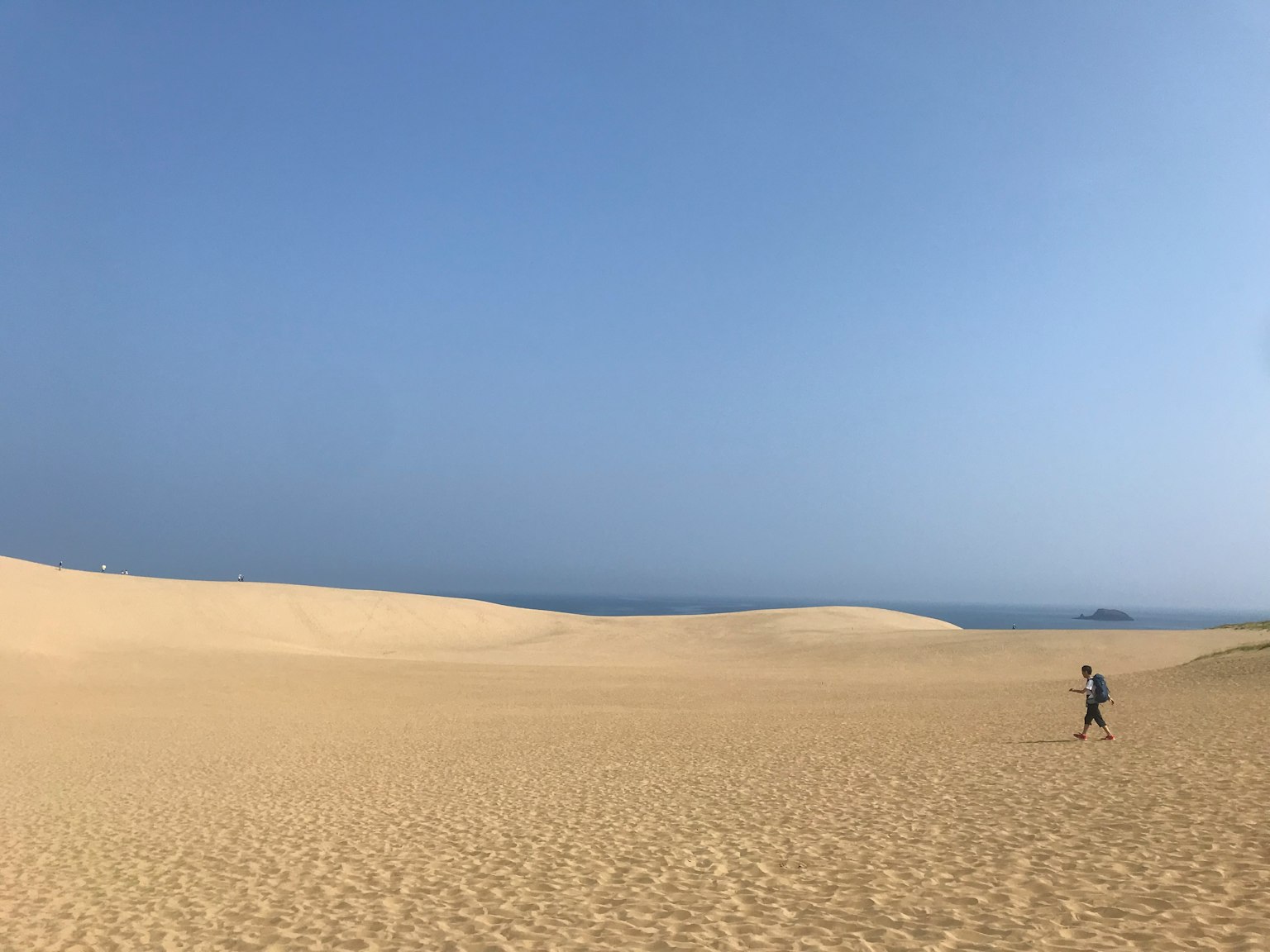広大な砂丘と青い空の風景に人が歩いている