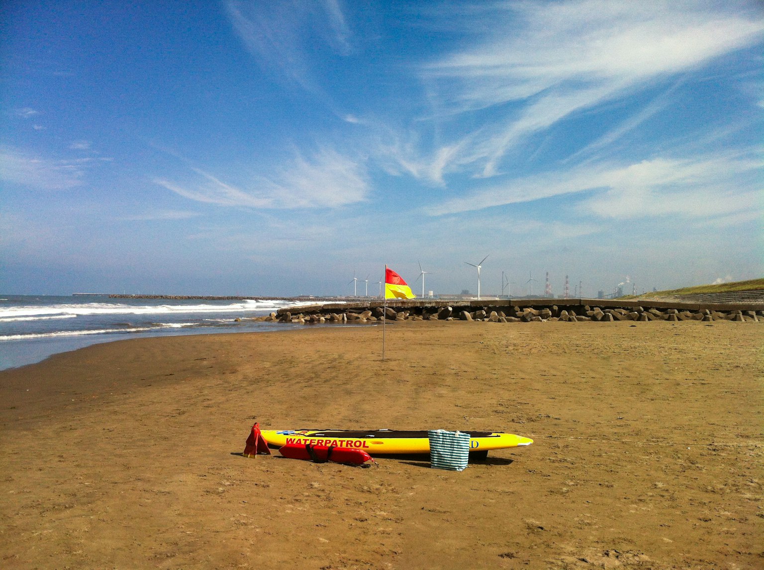 Papan selancar kuning dan pelampung merah di pantai di bawah langit biru dengan awan putih