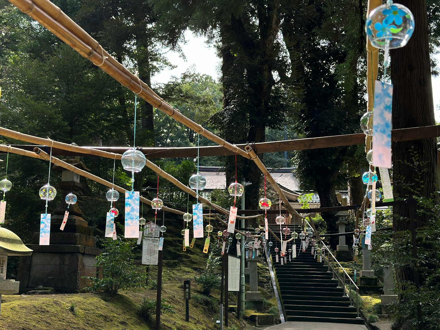 Una scena serena di un santuario con campane a vento e strisce colorate appese a pali di bambù circondati da una vegetazione lussureggiante