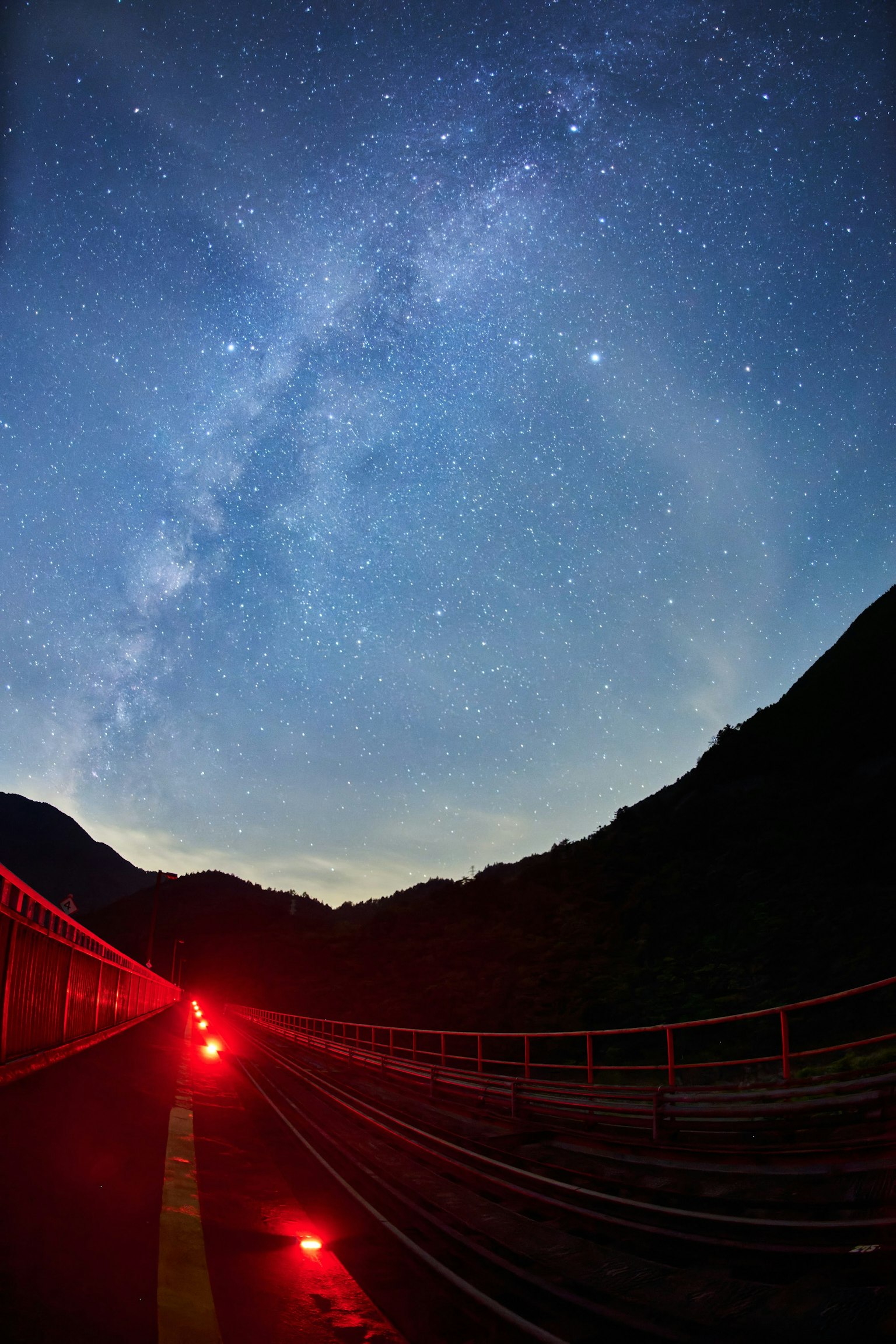 Mountain path with red lights under a starry sky featuring the Milky Way