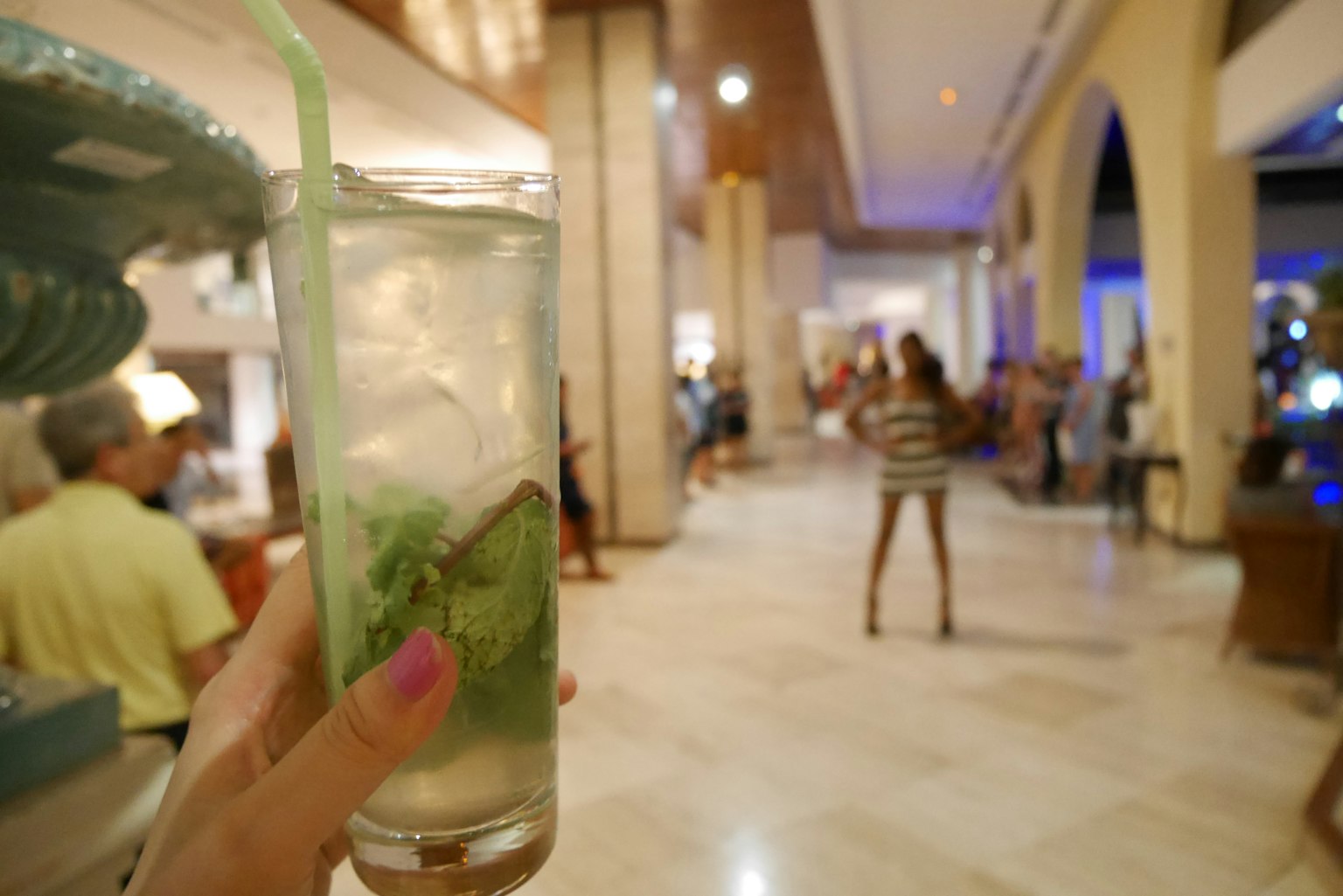 Eine Hand hält einen Mojito mit einer Lounge und Leuten im Hintergrund