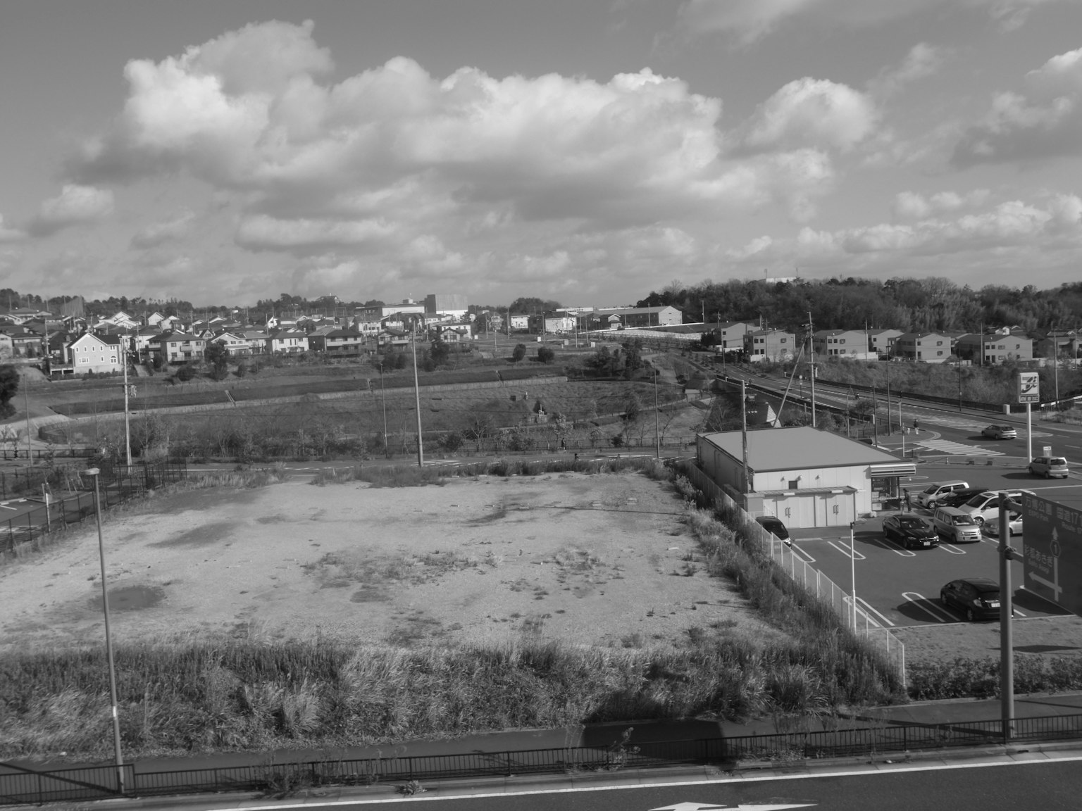 Terrain vacant avec un quartier résidentiel environnant sous un ciel clair et des nuages