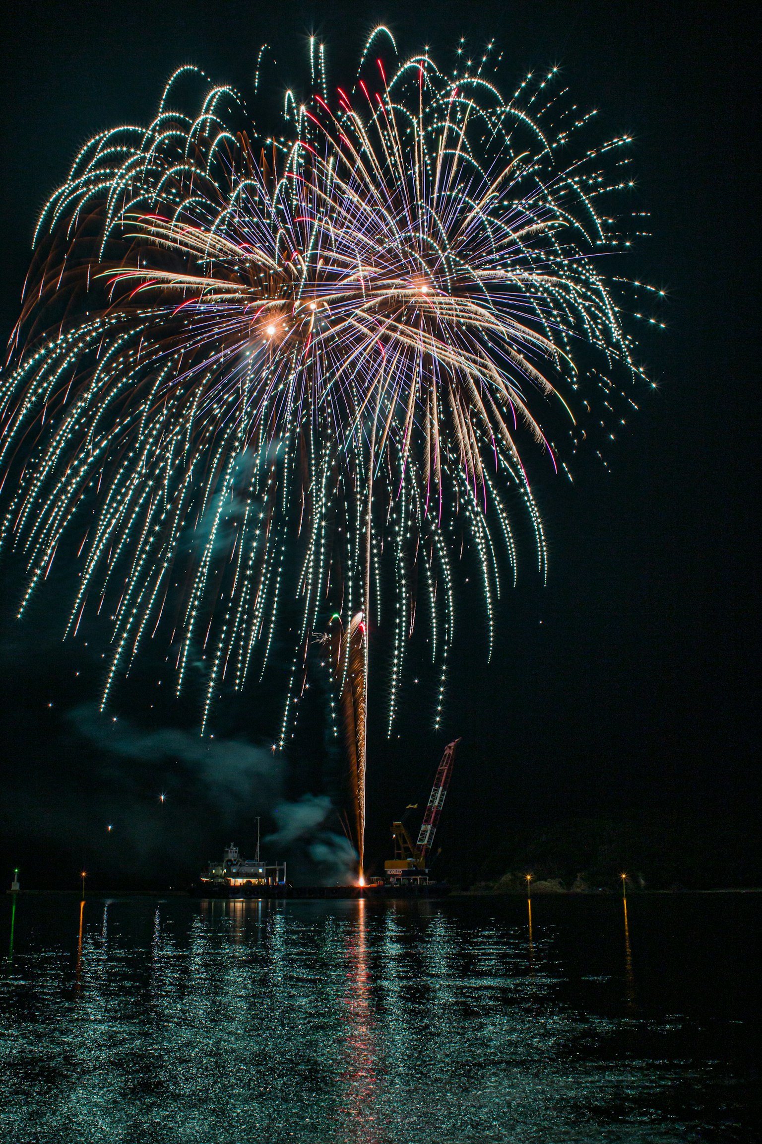 Colorful fireworks bursting in the night sky reflecting on the water surface