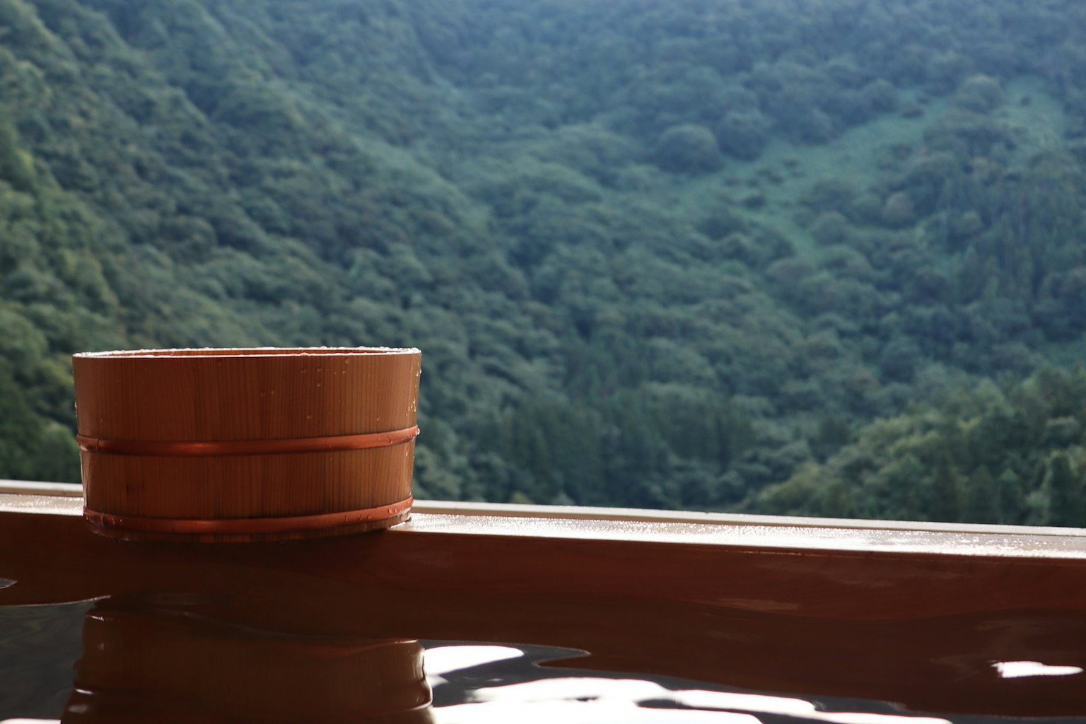 Tina de madera con vista a montañas verdes en un entorno de manantial caliente