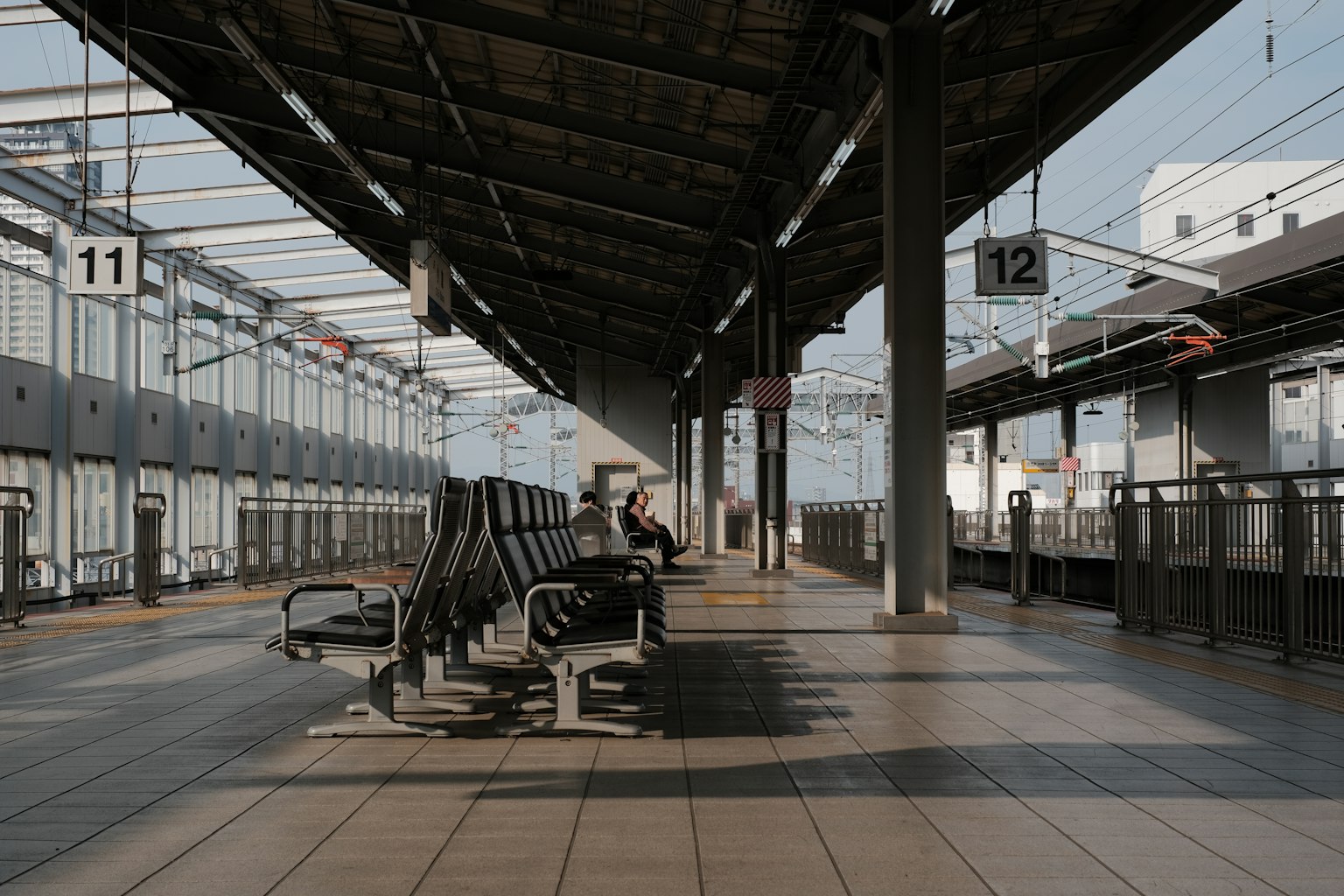 Plataforma de tren tranquila con una persona sentada y paneles de salida de tren