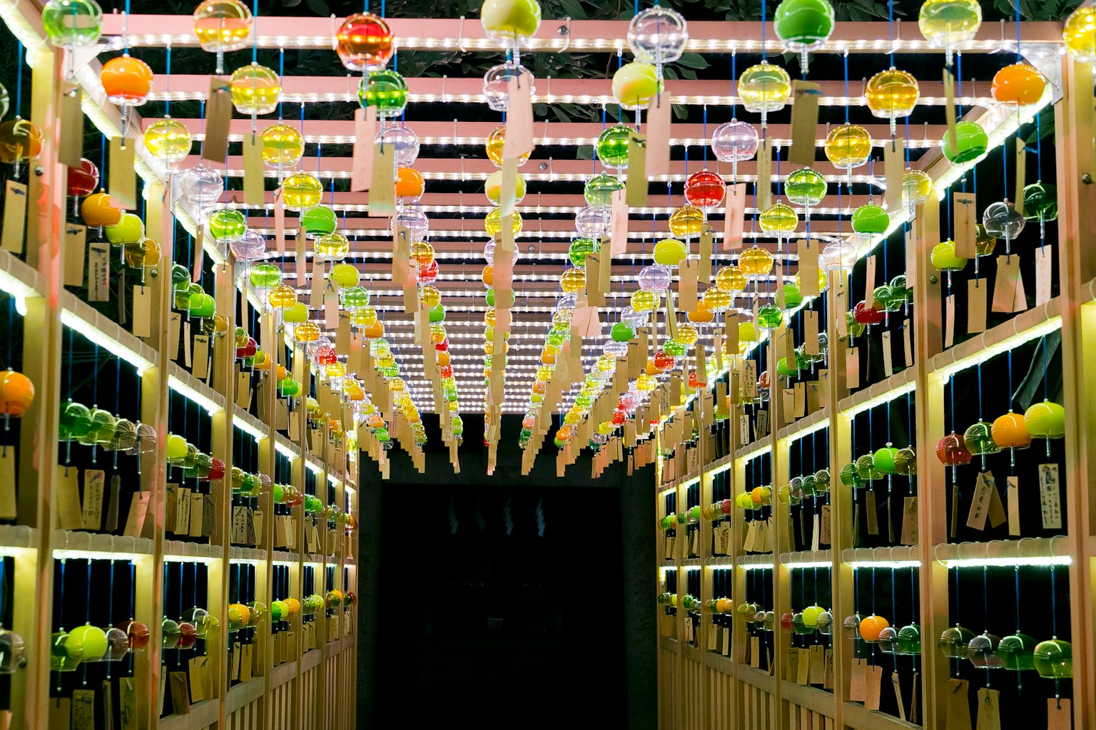 Un espace en forme de tunnel avec des bouteilles de vin alignées et des décorations de fruits colorés suspendues au plafond