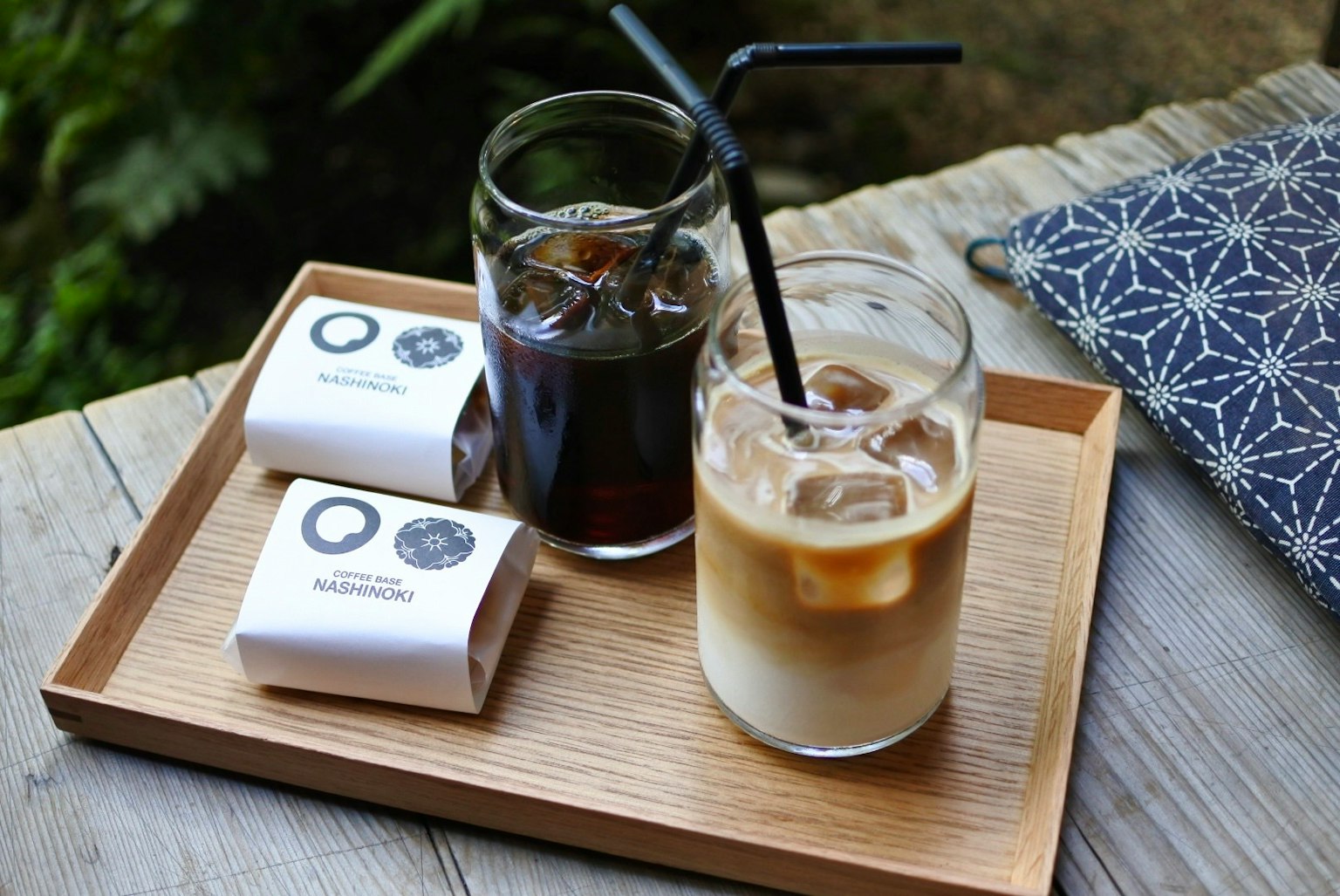 A wooden tray with iced coffee and hot coffee served with desserts