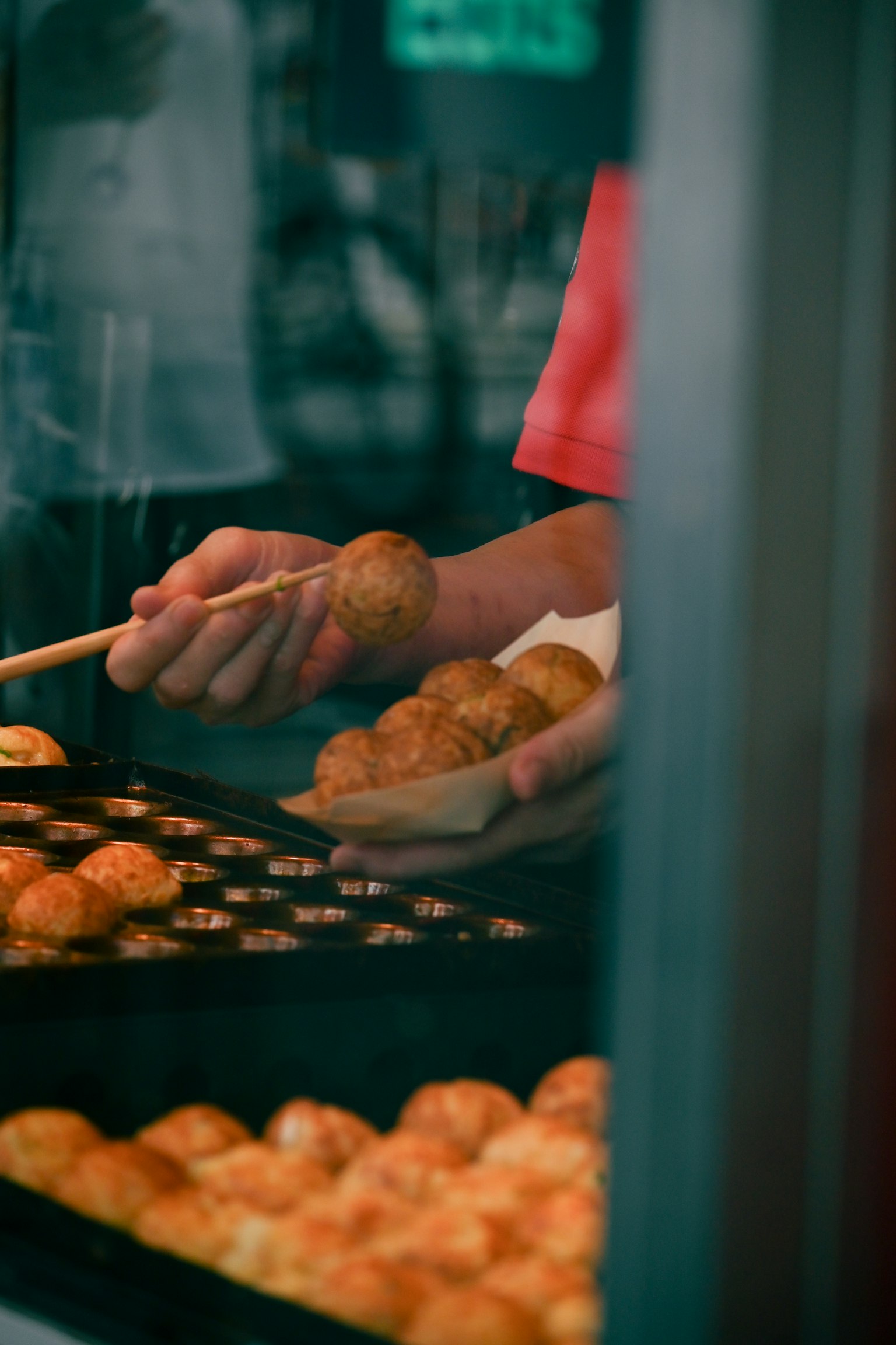 Vendedor sirviendo takoyaki con palillos desde un puesto de comida callejera