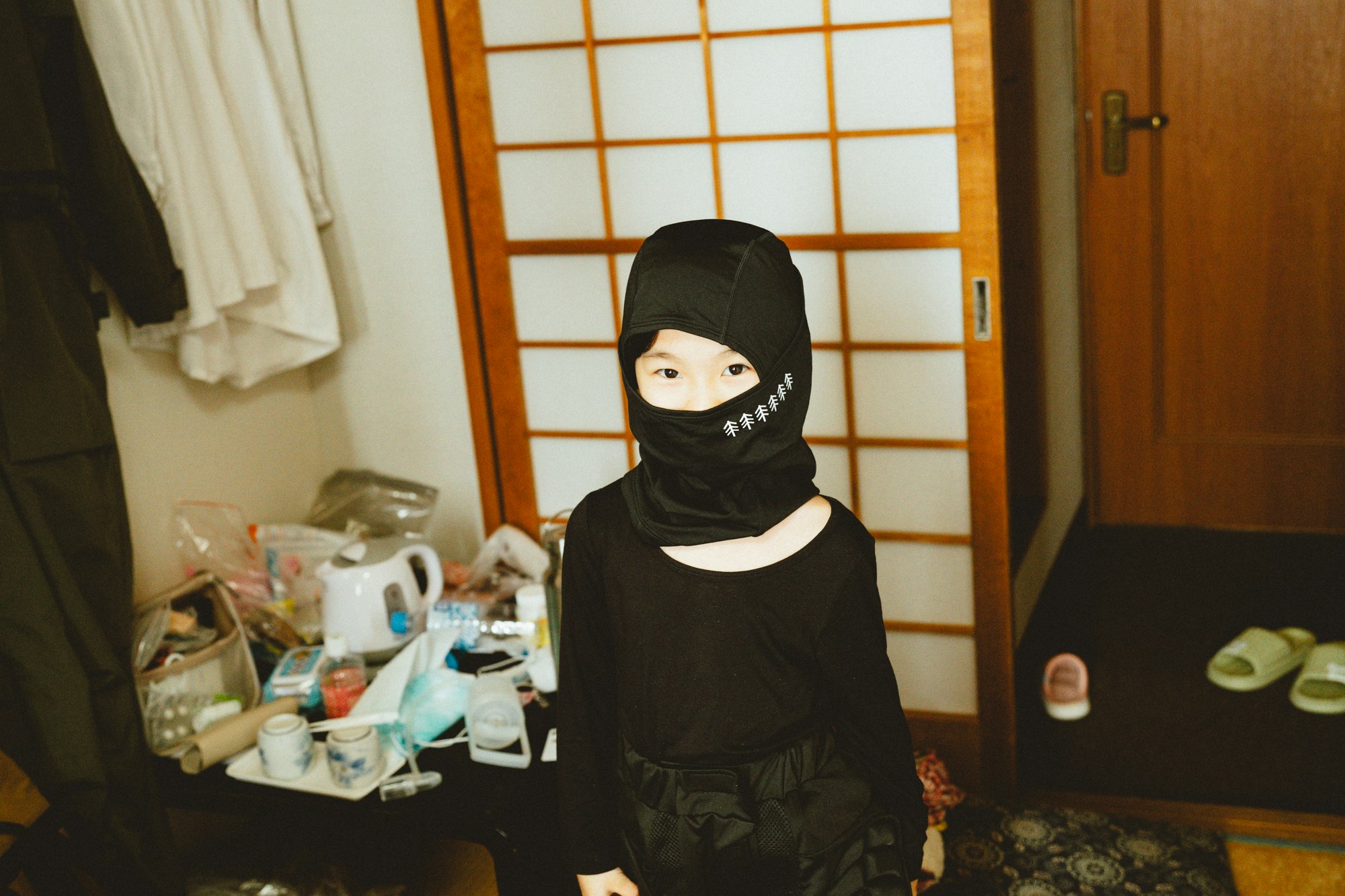 和室の部屋でテーブルの前に立つ黒い覆面の人物