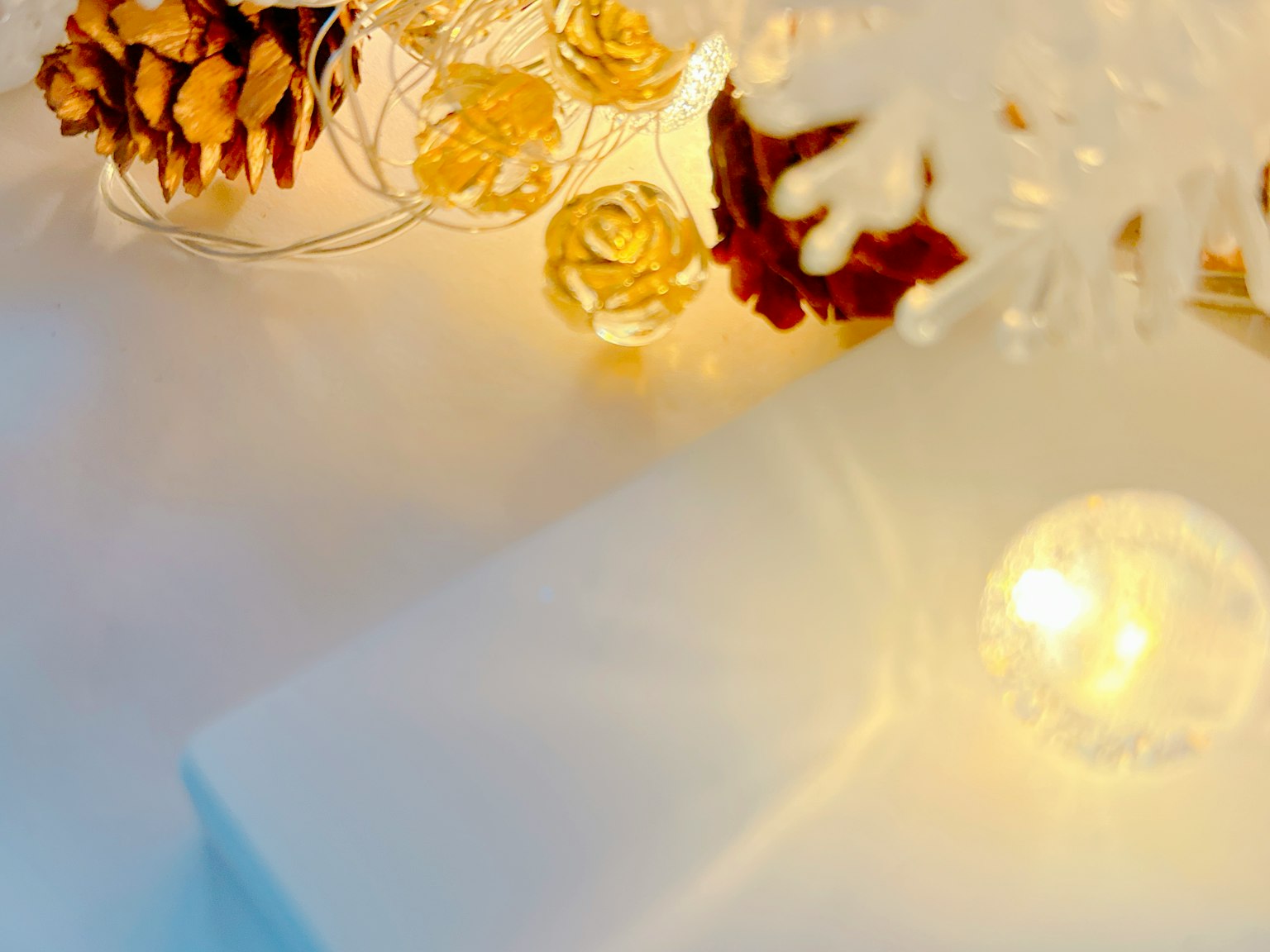 Decoración navideña con flores doradas y piñas sobre un fondo blanco