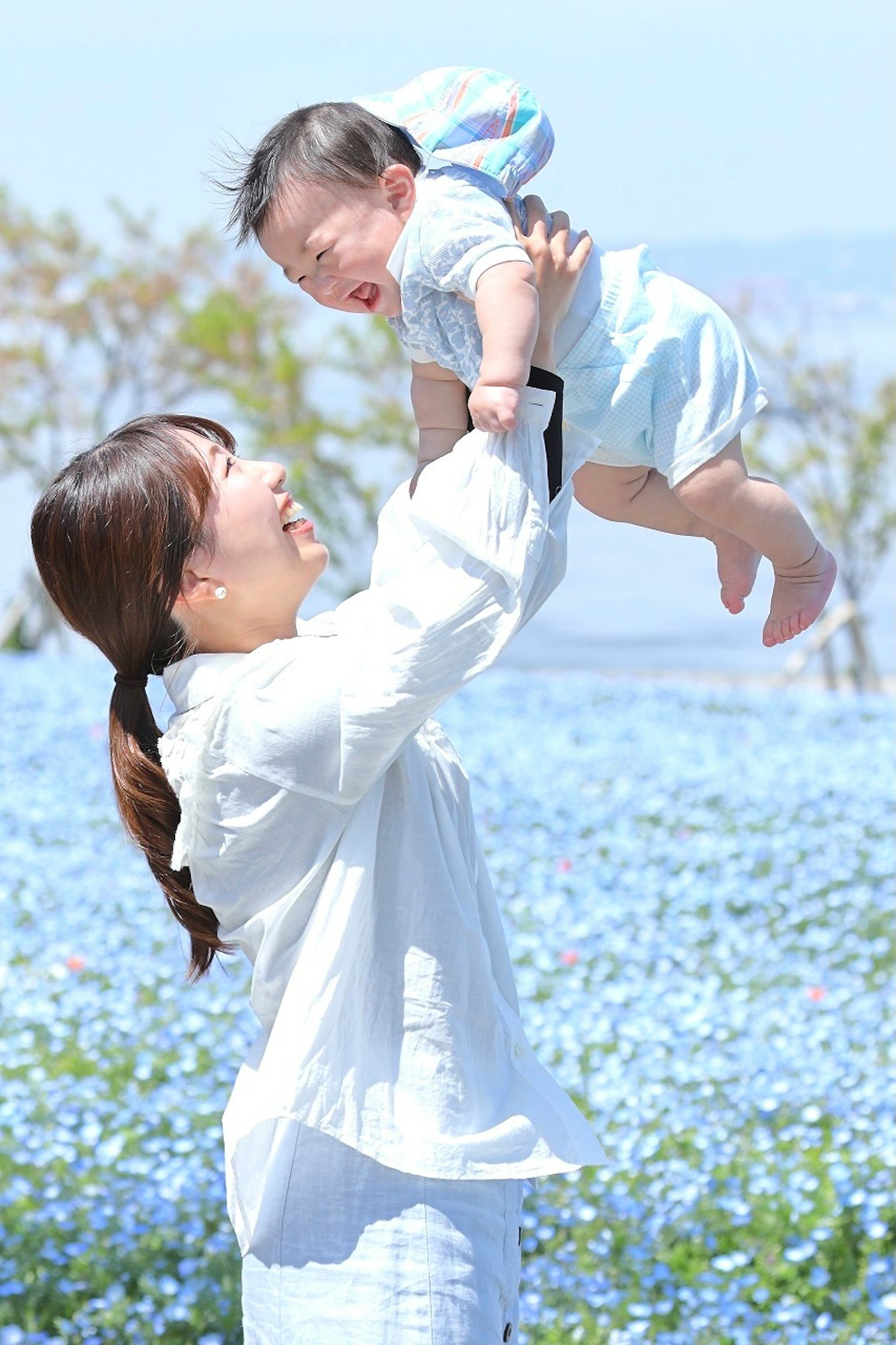 Mẹ vui vẻ nâng em bé trong cánh đồng hoa màu xanh