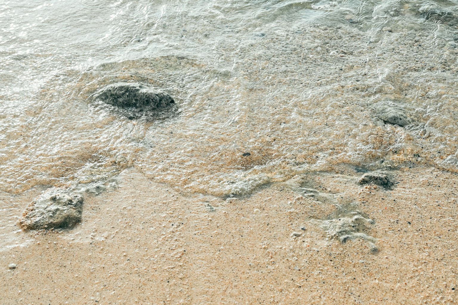 海浪拍打沙滩，黑色岩石可见