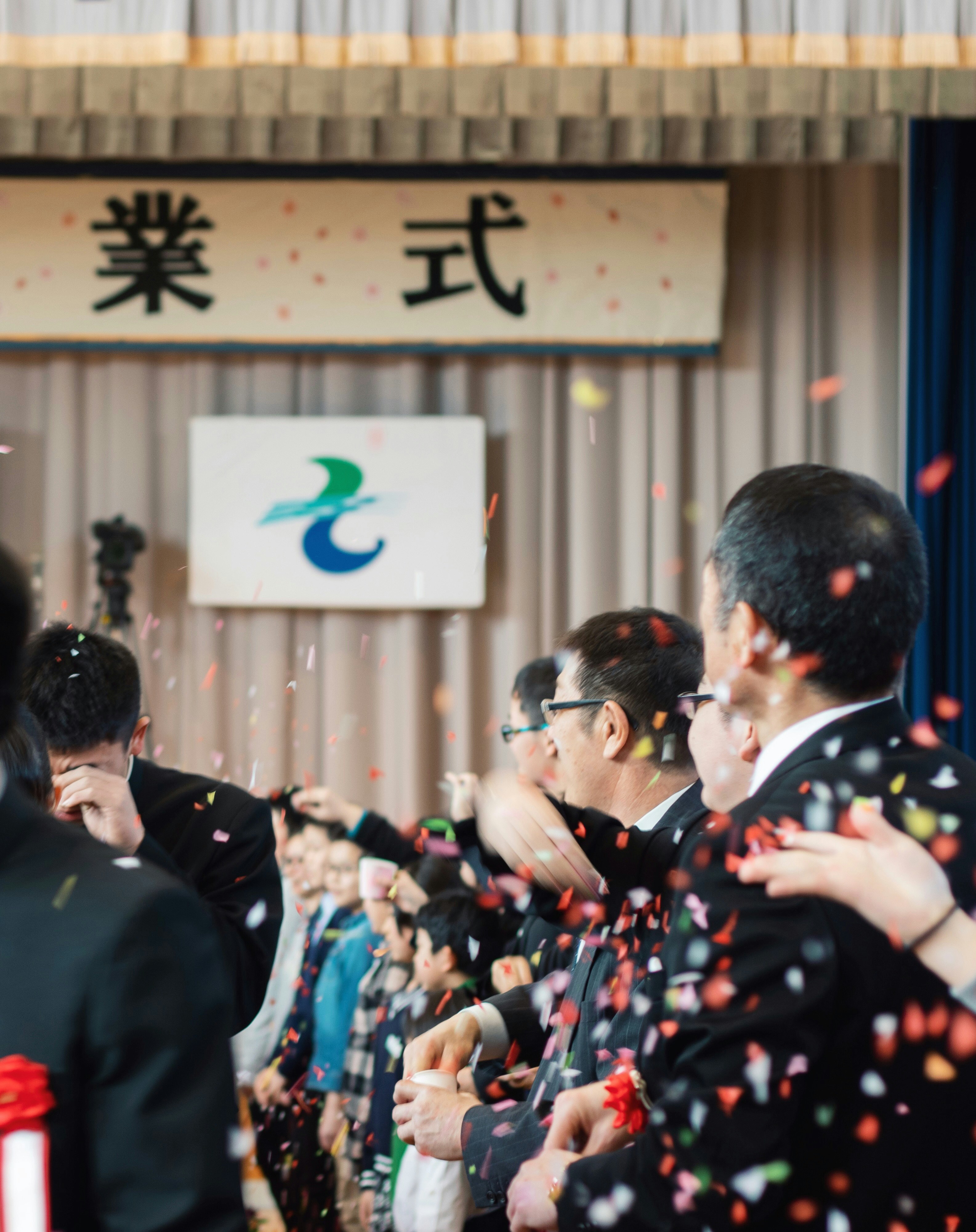 紙吹雪の中で手を振るスーツ姿の人々の式典会場