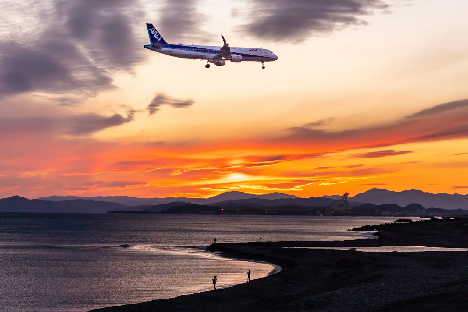 Airplane landing against a vibrant sunset over the ocean
