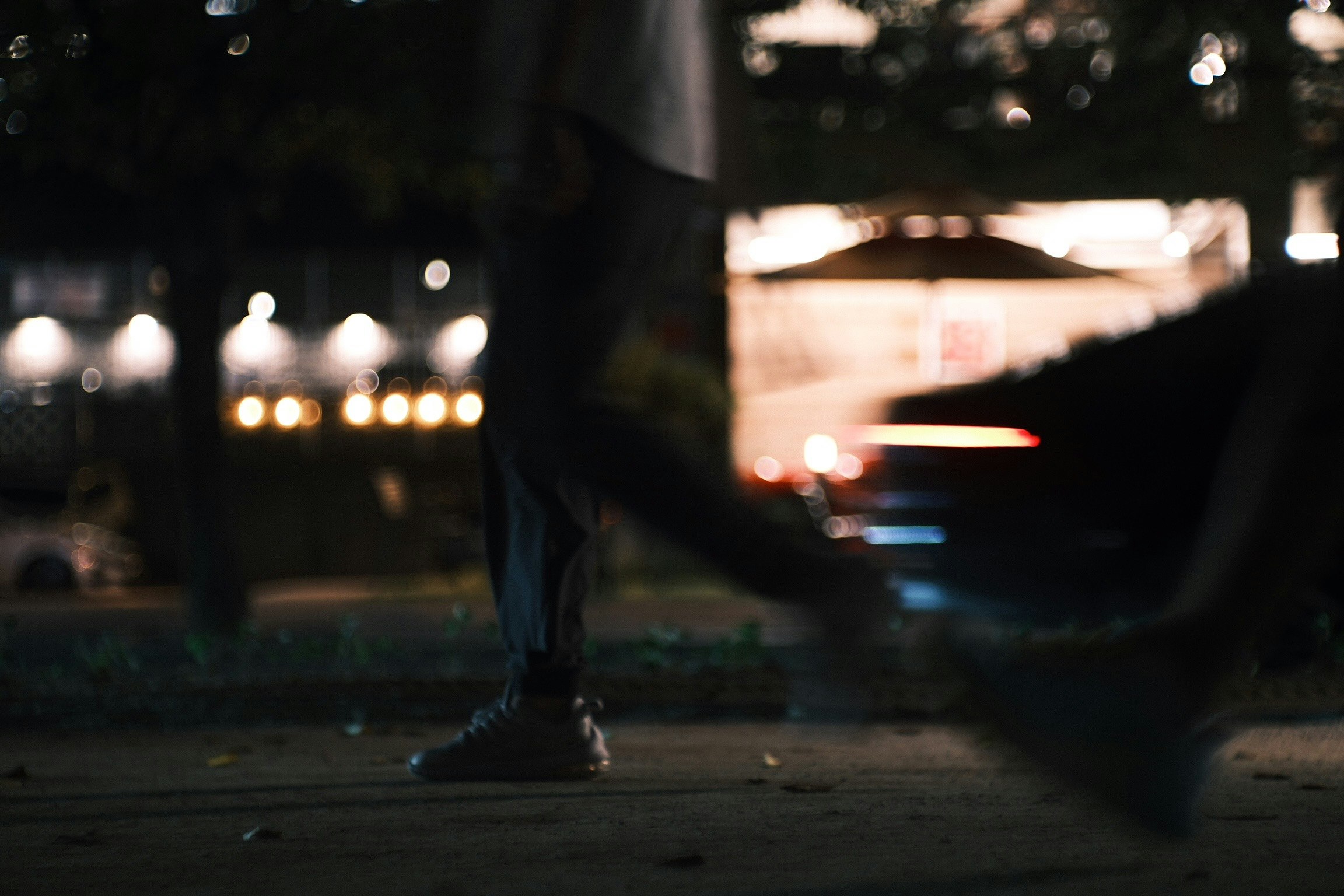 夜の路上で歩く人の足元と街のにじむ光