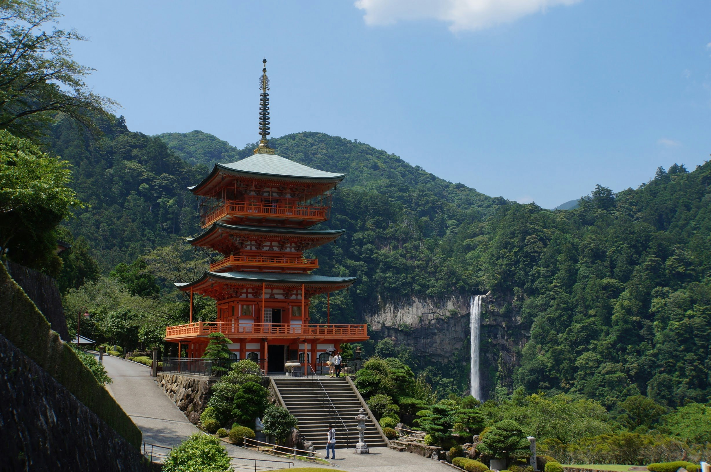 Scenic temple view with a vermilion pagoda and waterfall surrounded by green mountains