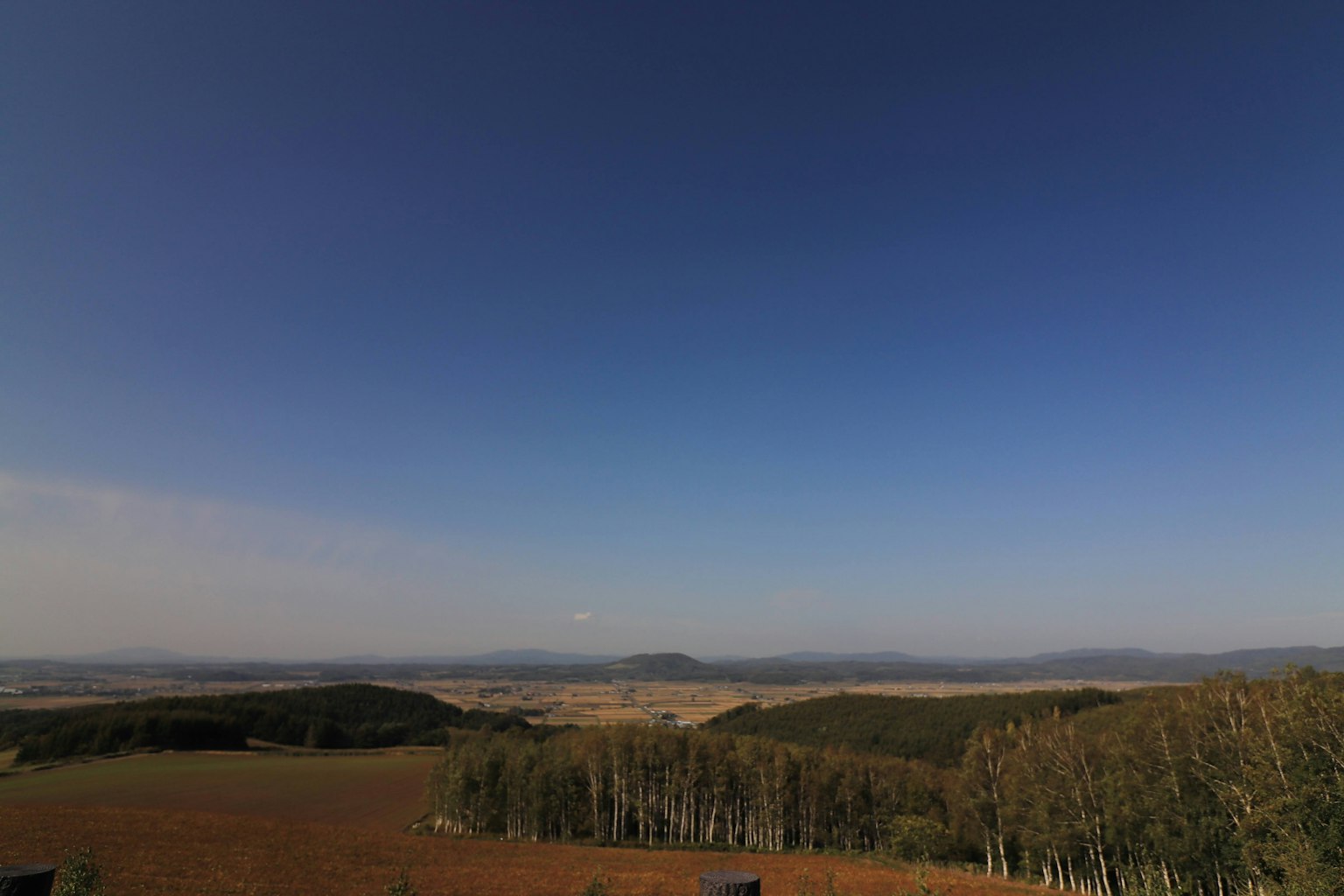 Panoramic view featuring a blue sky and vast landscape with low hills and open fields