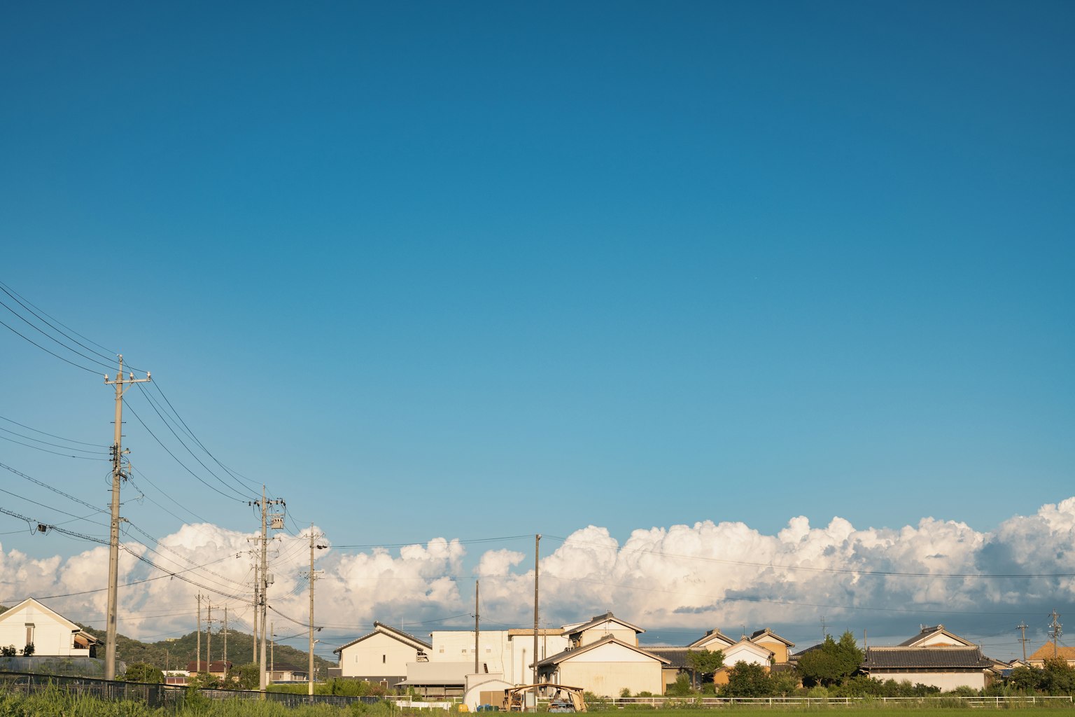 Paesaggio rurale con cielo blu e nuvole bianche, con pali elettrici e case