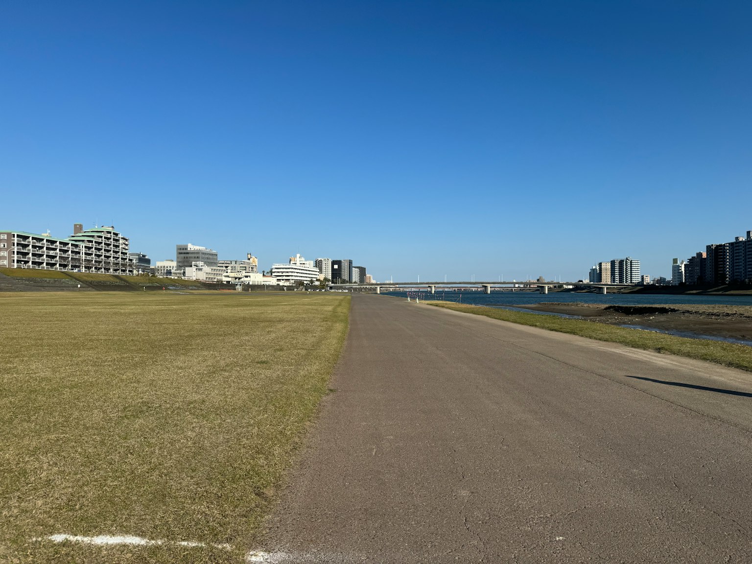 Un chemin au bord de la rivière et une zone herbeuse sous un ciel bleu clair