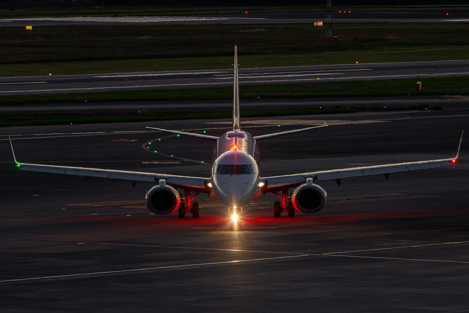 Frontansicht eines Flugzeugs auf einer Flughafenlandebahn mit beleuchteten Lichtern in der Nacht