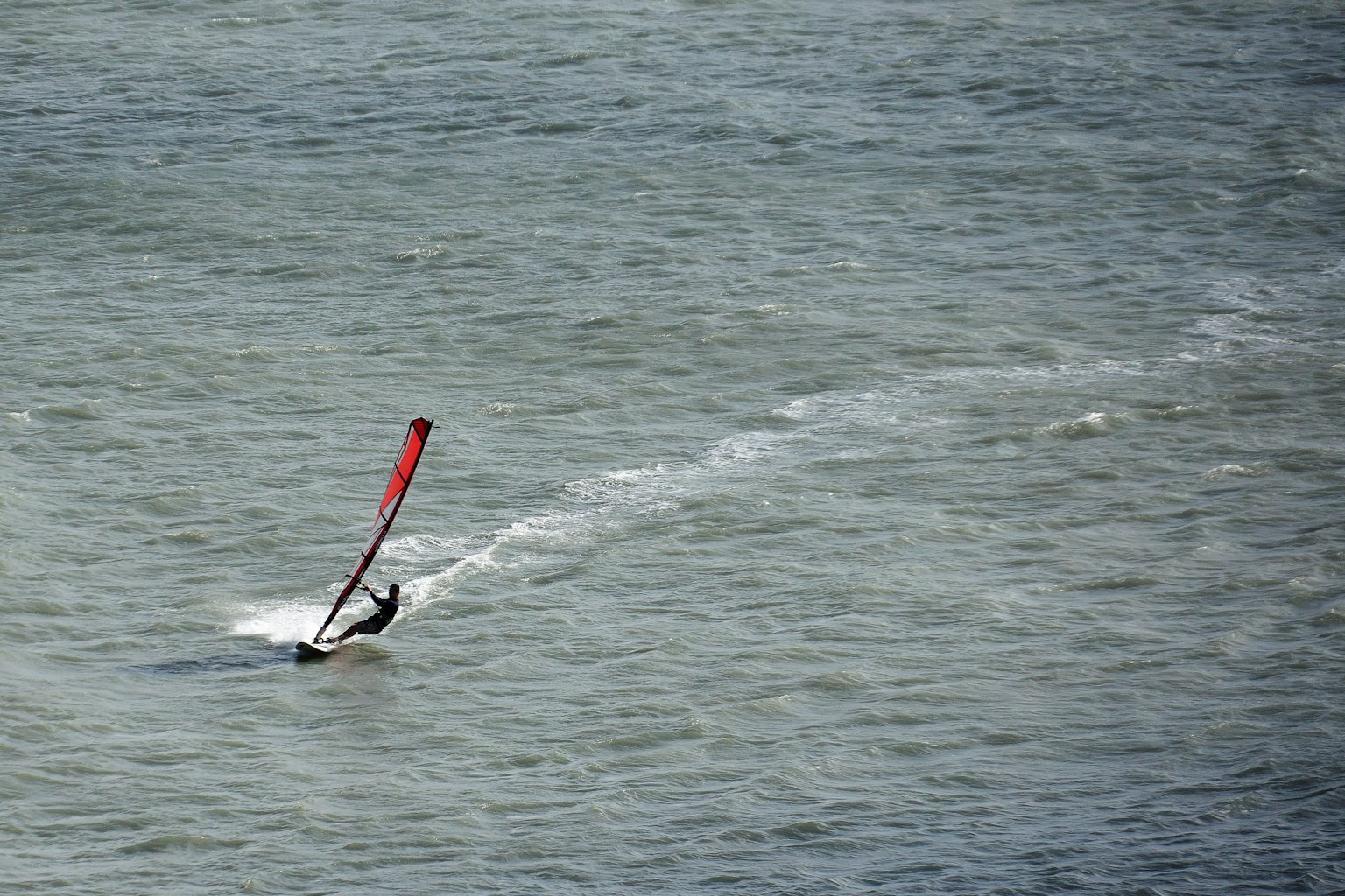 Ein Windsurfer, der über das Wasser gleitet mit einem roten Segel