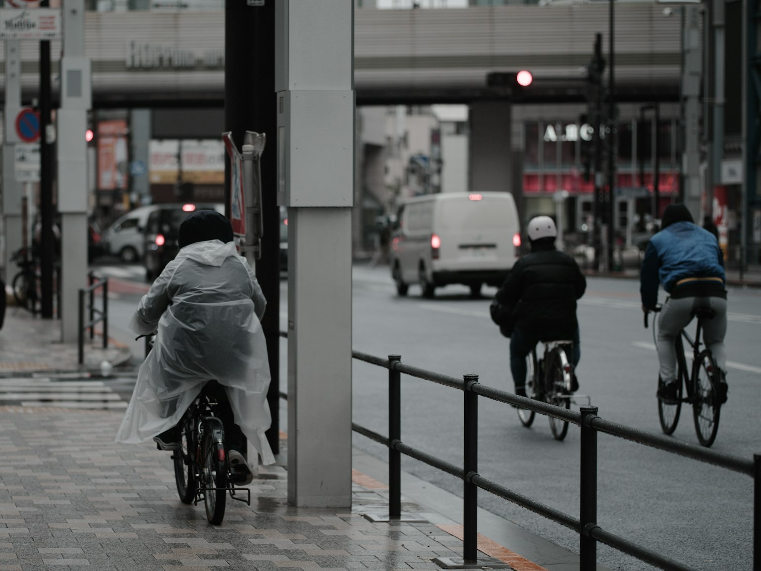 Personas montando bicicletas bajo la lluvia con un fondo urbano y semáforos visibles