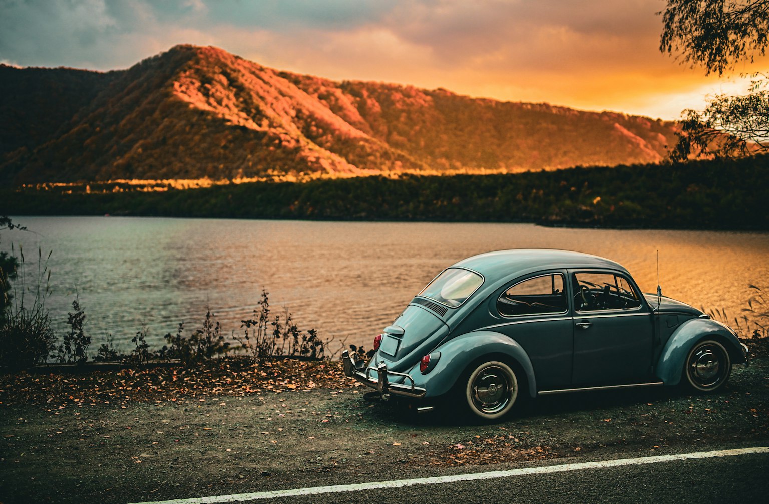 美しい夕焼けの湖のそばに停まっている青いビートル車