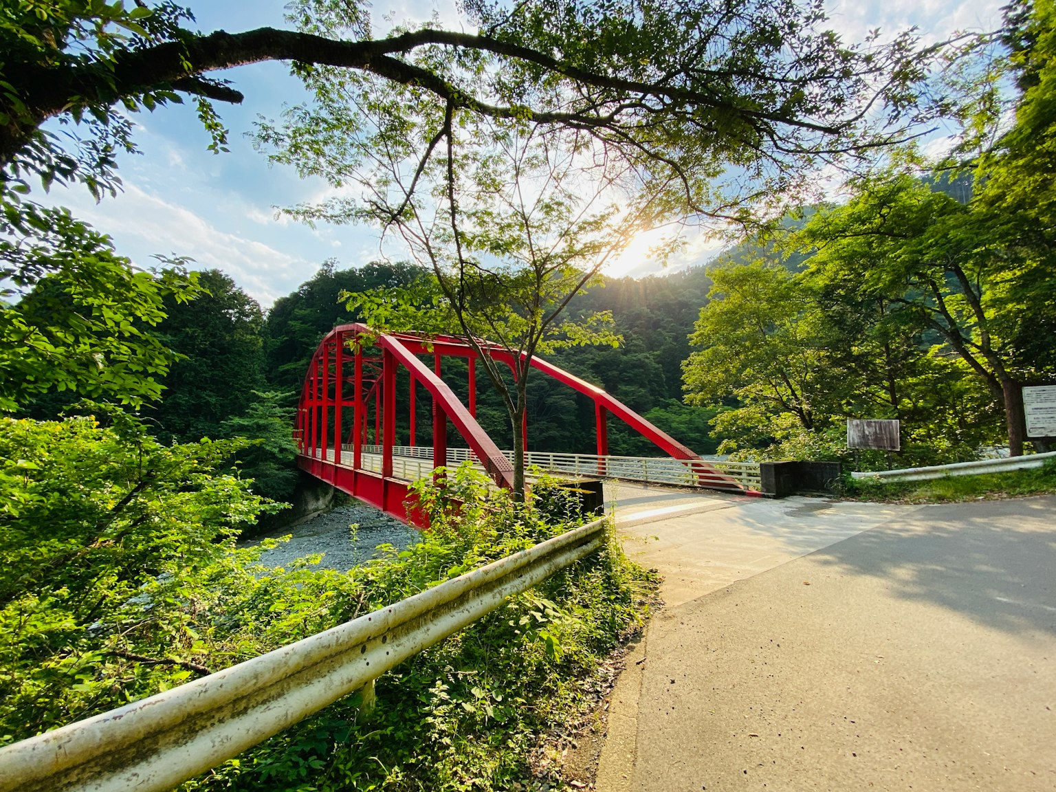 Pont en arc rouge entouré d'arbres verts avec une lumière vive
