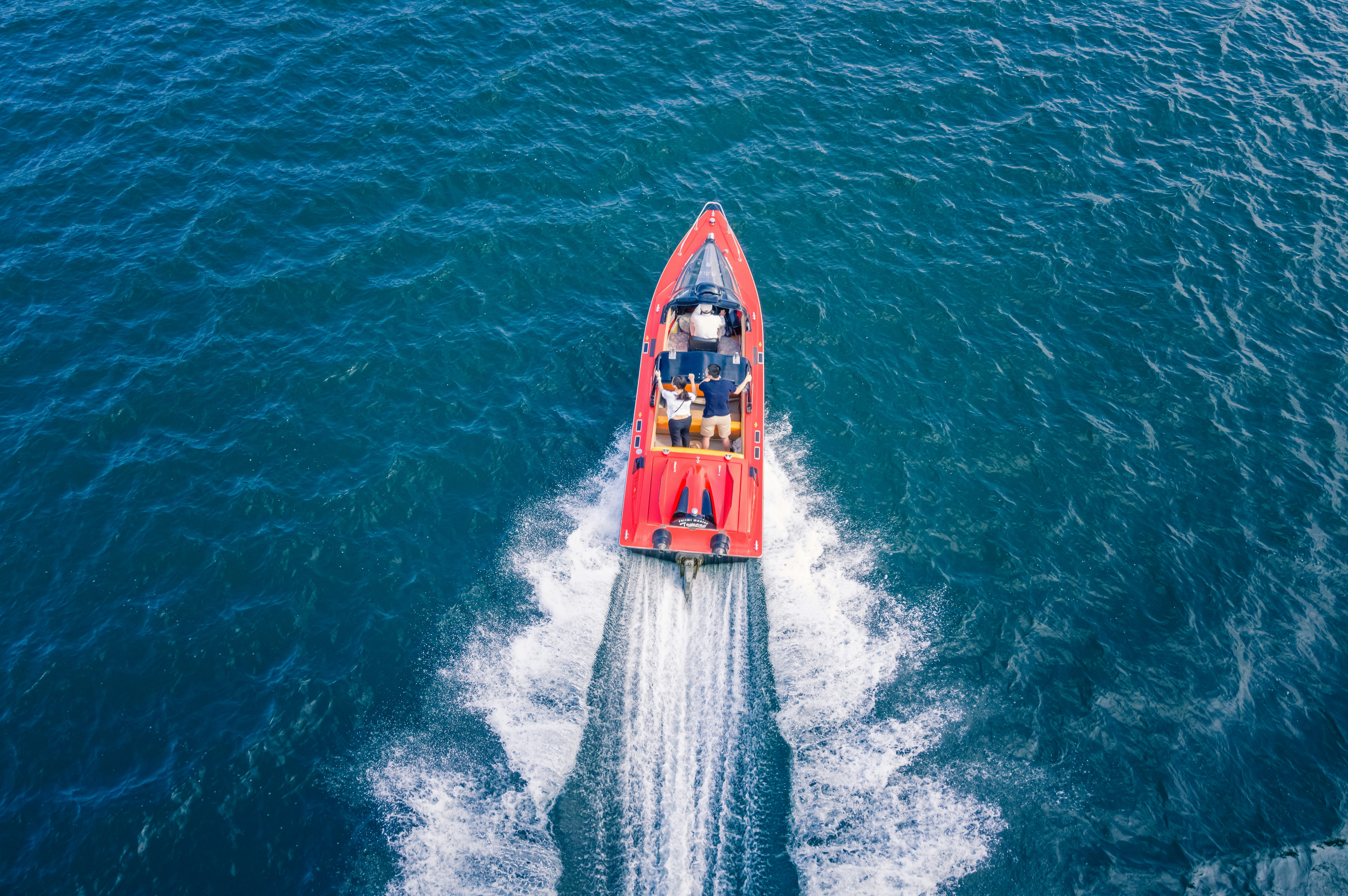 Rotes Boot, das durch blaues Wasser aus der Vogelperspektive fährt