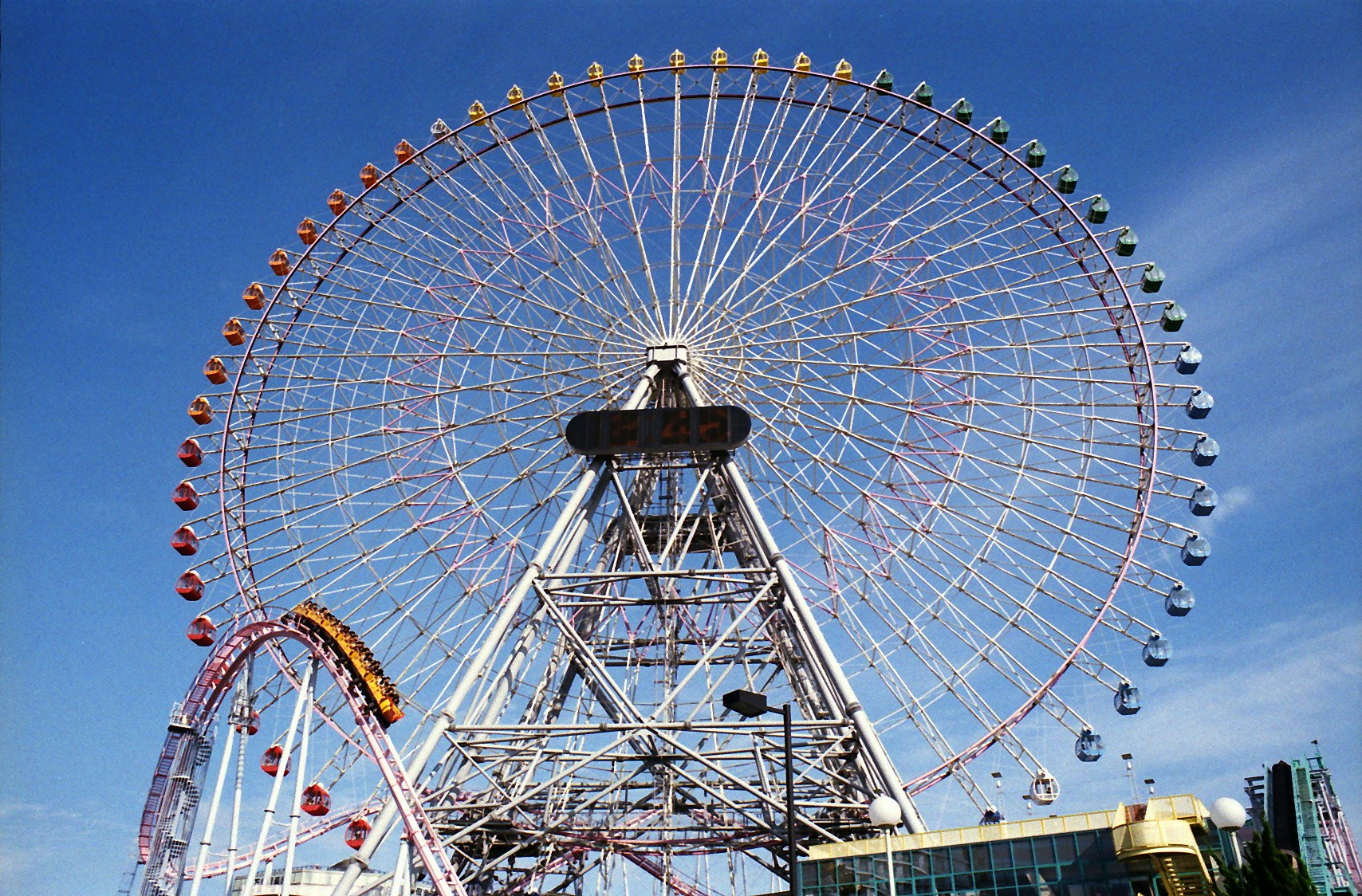 青空の下にそびえる観覧車と遊園地のアトラクション